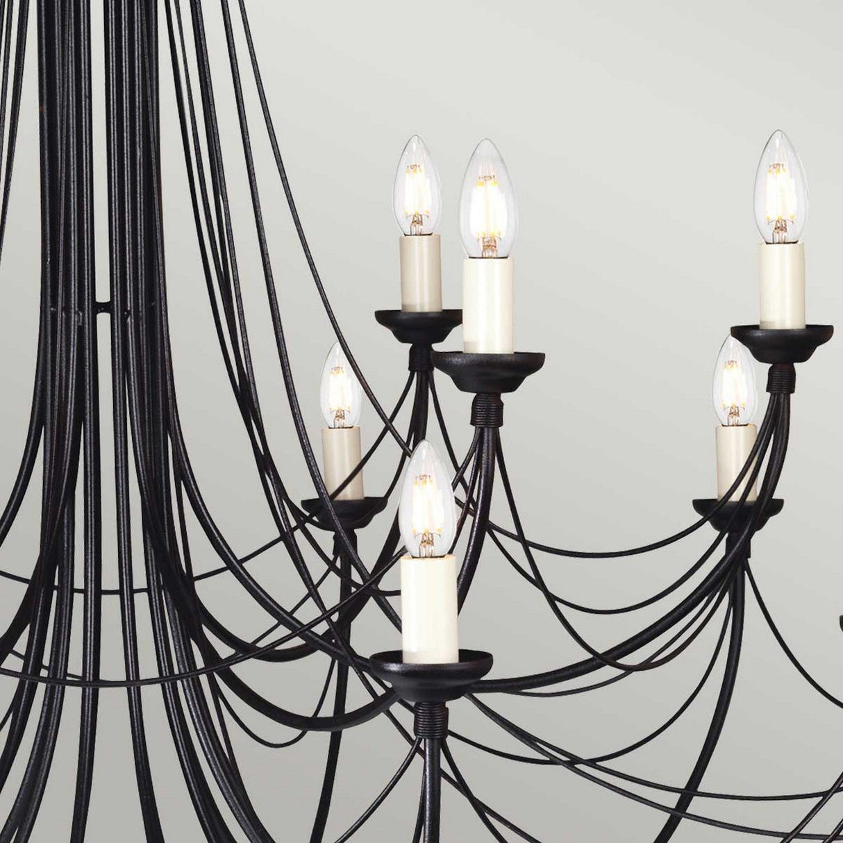 Close-up of the Carisbrooke 18 Light Chandelier in black, featuring elegant candelabra-style arms with candle-shaped light bulbs. The curved design forms a sophisticated and intricate pattern, reminiscent of a Gothic-inspired chandelier, set against a neutral background.