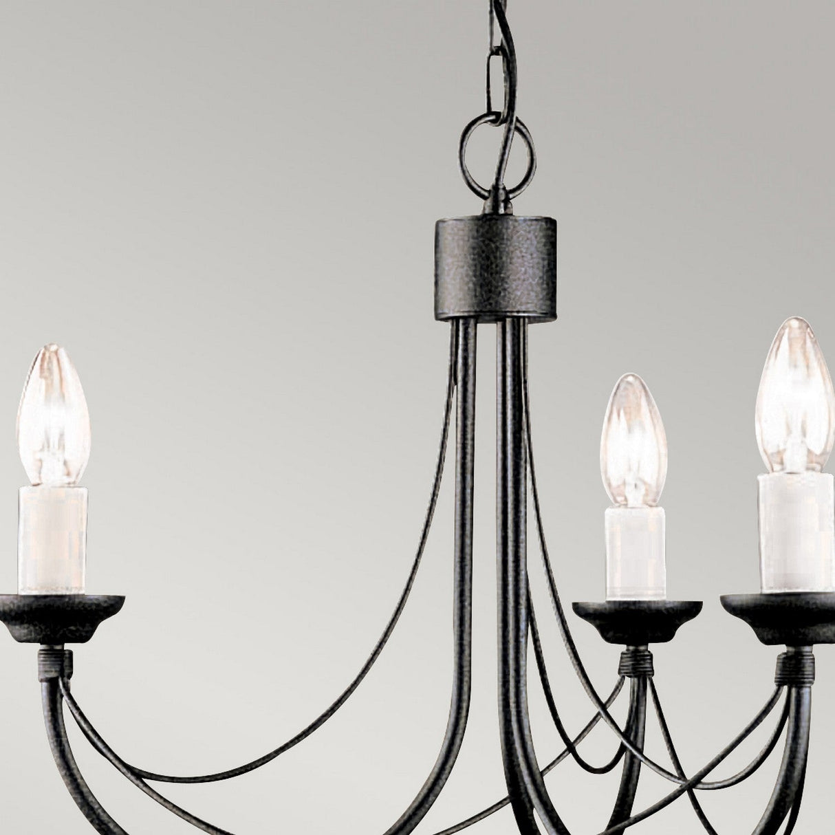 A Carisbrooke 3 Light Chandelier in black hangs against a light gray background, showcasing its candelabra-style silhouette. This elegant design features three candle-shaped light bulbs, gracefully curved metal arms, and a central chain for suspension.