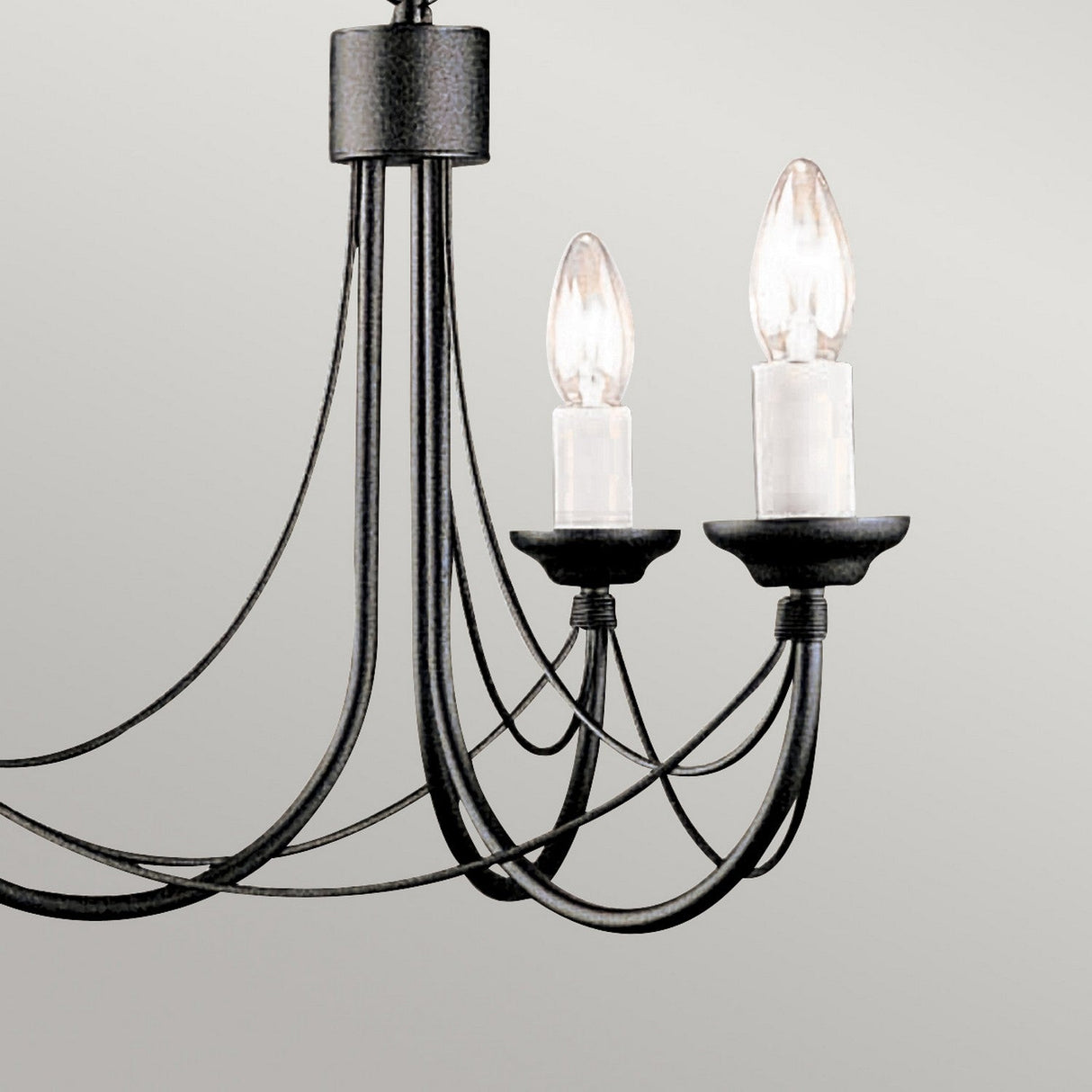 A close-up of the Carisbrooke 3 Light Chandelier showcases its Gothic-inspired design, complete with black metal, two candle-style light bulbs, and elegantly curved arms set against a light gray background.
