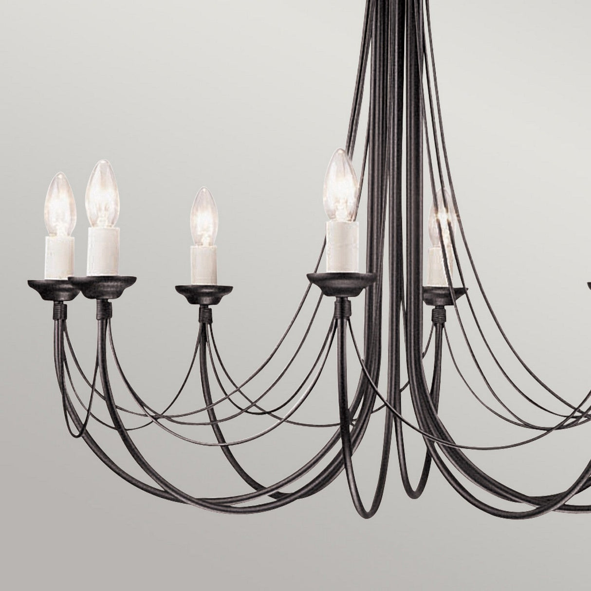The Carisbrooke 8 Light Chandelier - Black combines modern design with a hint of vintage charm, showcasing multiple black metal arms and eight candle-like light bulbs. Its elegant, curved lines in a minimalist style add a touch of Gothic-inspired beauty against a plain setting.
