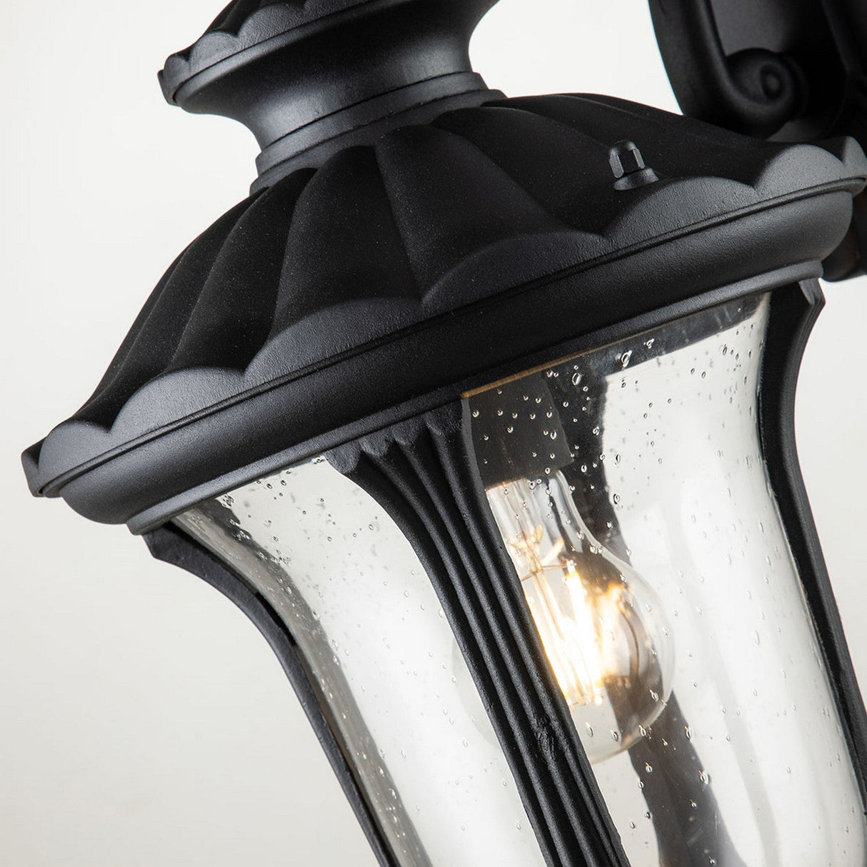 A close-up of the Chicago Outdoor Small Wall Lantern in black highlights its textured, speckled glass casing that radiates a sense of vintage elegance. The robust aluminum frame brings a classic touch to this fixture, beautifully showcasing a bulb with timeless charm.