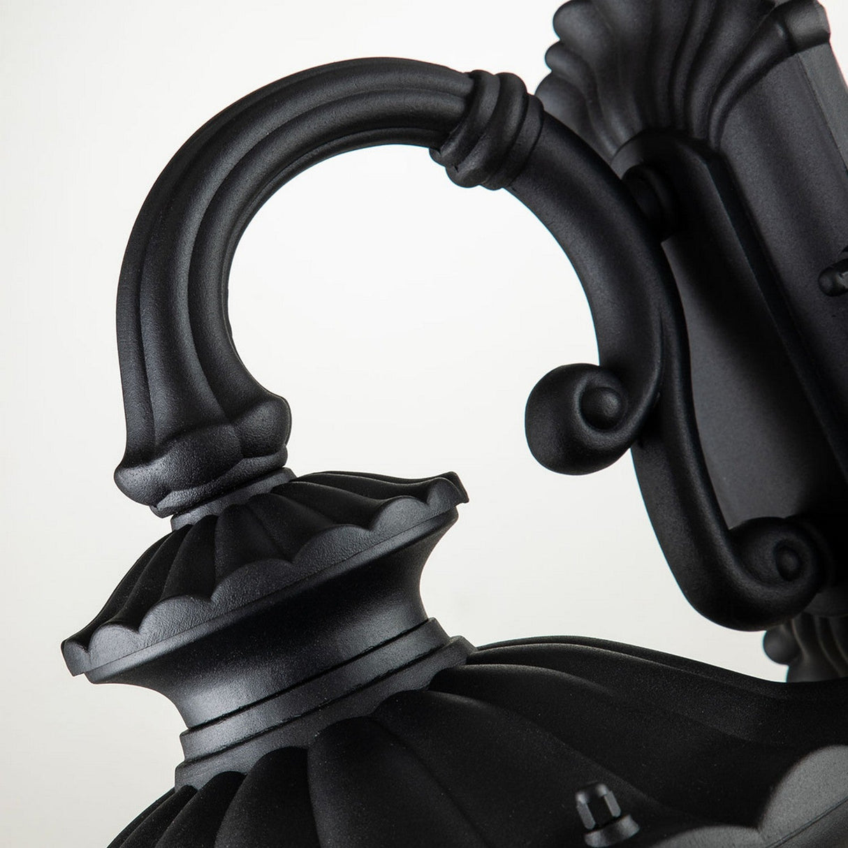 Close-up of a Chicago Outdoor Small Wall Lantern - Black, exuding vintage elegance with its ornate scrollwork and scalloped design. Crafted from durable aluminum, it stands as a stunning decorative black piece against a plain background.