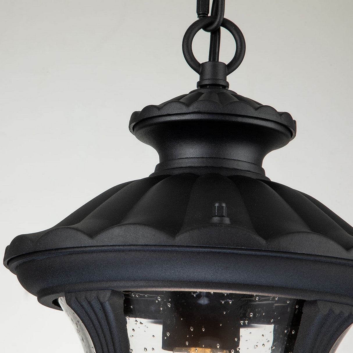 A detailed look at the Chicago Outdoor 1 Light Small Chain Pendant in Black showcases its vintage charm through a rounded top and decorative finial. The clear seeded glass casing reveals a single light bulb inside, further enhanced by delicate water droplet textures on the surface.