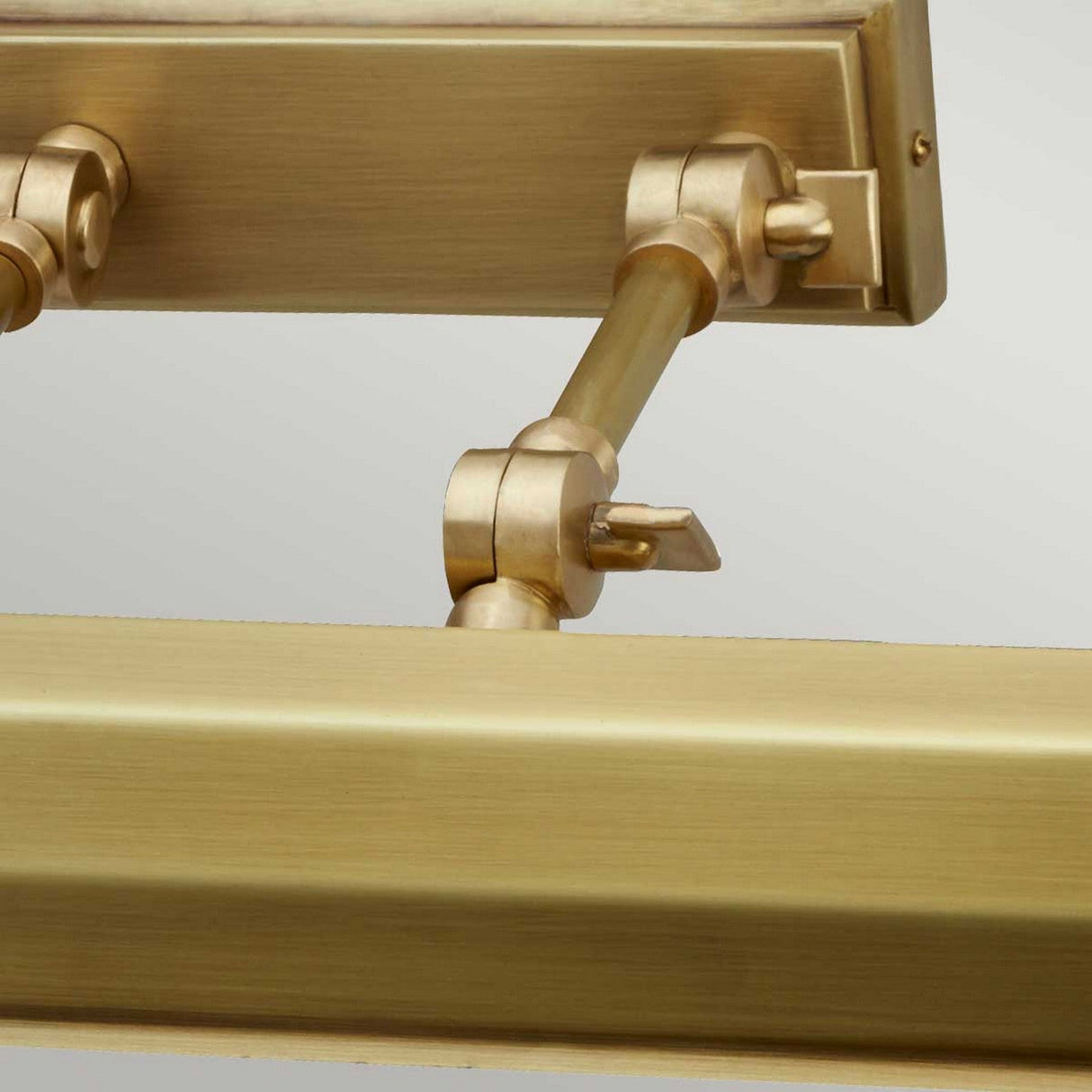 A close-up of the Chawton Large Picture Light - Aged Brass showcases its adjustable joints and rods, offering directional lighting against a light gray backdrop. This fixture effortlessly combines structural elegance with decorative charm.