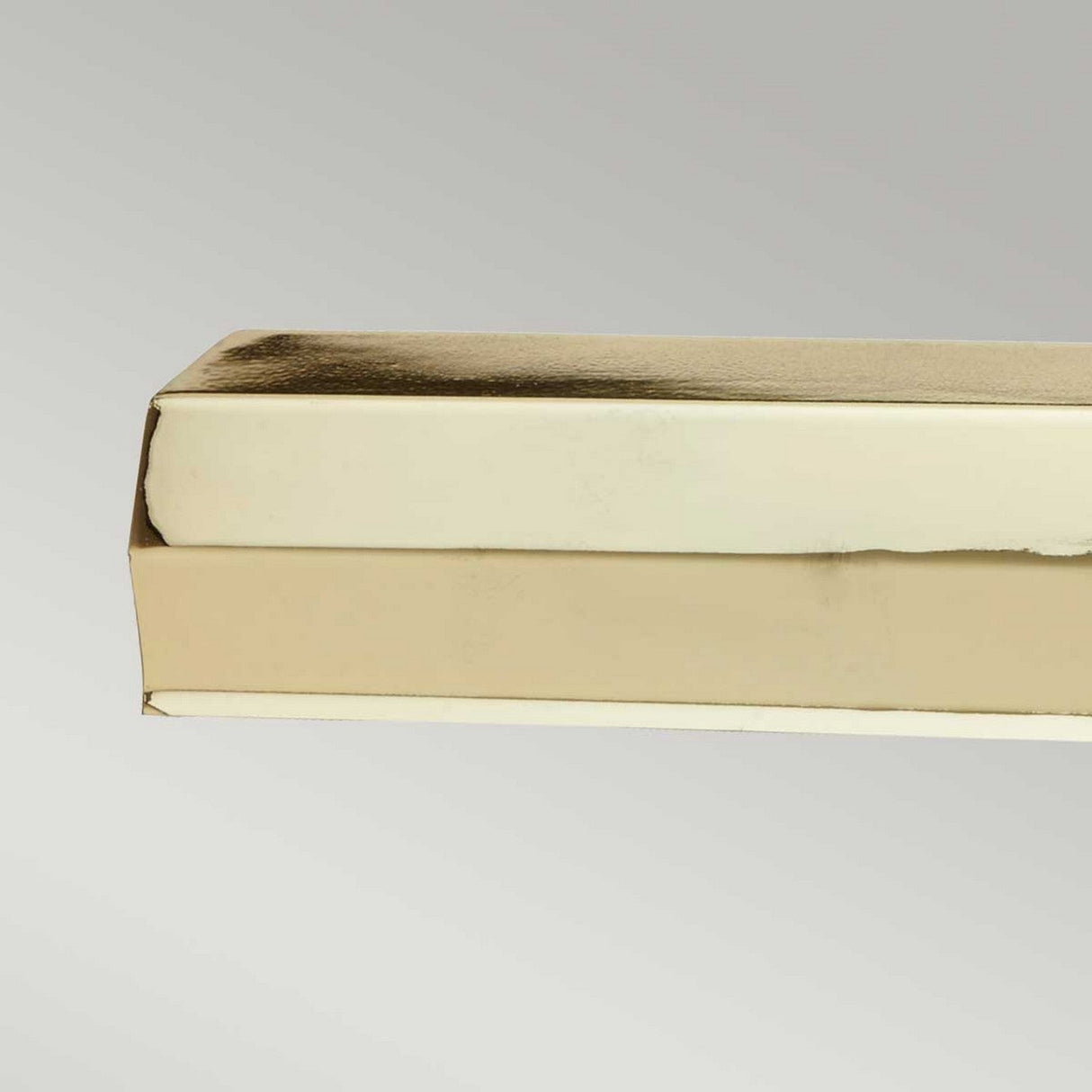 A stack of two closed books, featuring polished brass-colored pages, shines luxuriously against a plain gray background. The metallic luster is reminiscent of the elegant sheen of the Chawton Large Picture Light in Polished Brass, adding an air of sophistication.