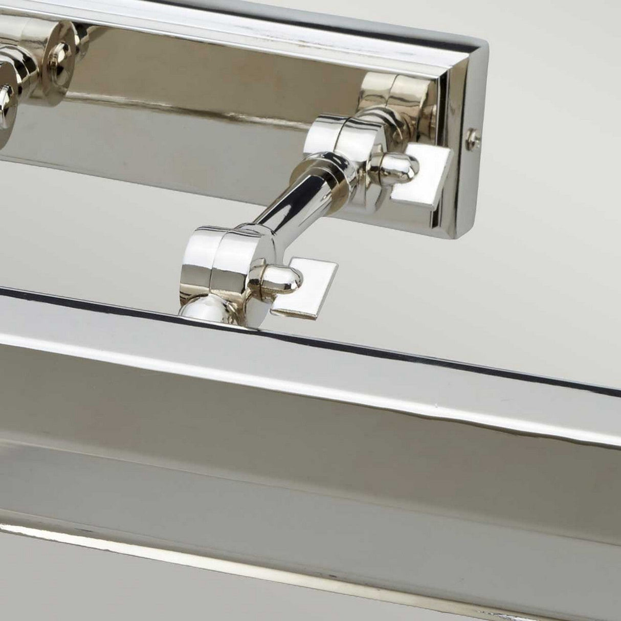 Close-up of the Chawton Large Picture Light in polished nickel, showcasing its adjustable wall sconce mount with articulated joints. This modern design features a rectangular base and horizontal arm, making it ideal for illuminating artwork. Its reflective surface adds an elegant touch to any space.