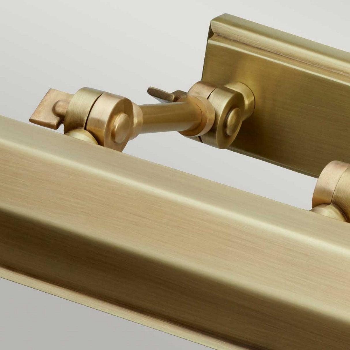 A close-up of the Chawton Medium Picture Light in aged brass reveals its sleek, modern design. The image highlights the detailed hinge and adjustable knuckle joints, emphasizing its functionality and elegant finish against a neutral background.