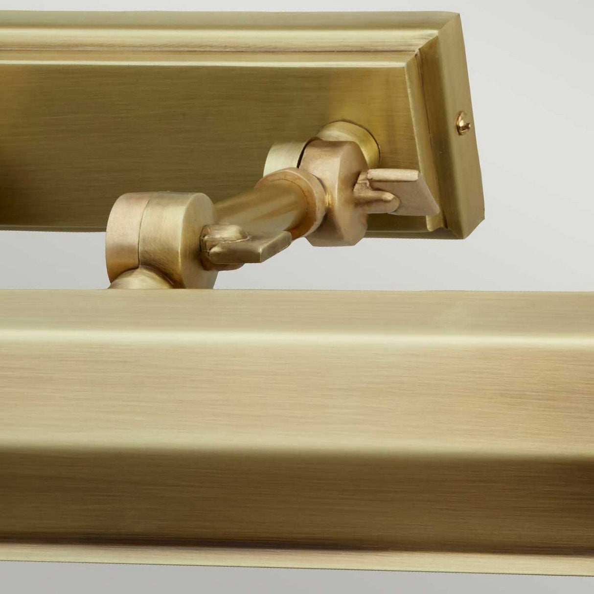 Close-up of the Chawton Medium Picture Light in aged brass, showcasing its metallic hinge mechanism with adjustable knuckle joints and screws, attached to a matching rectangular frame piece on a neutral background.