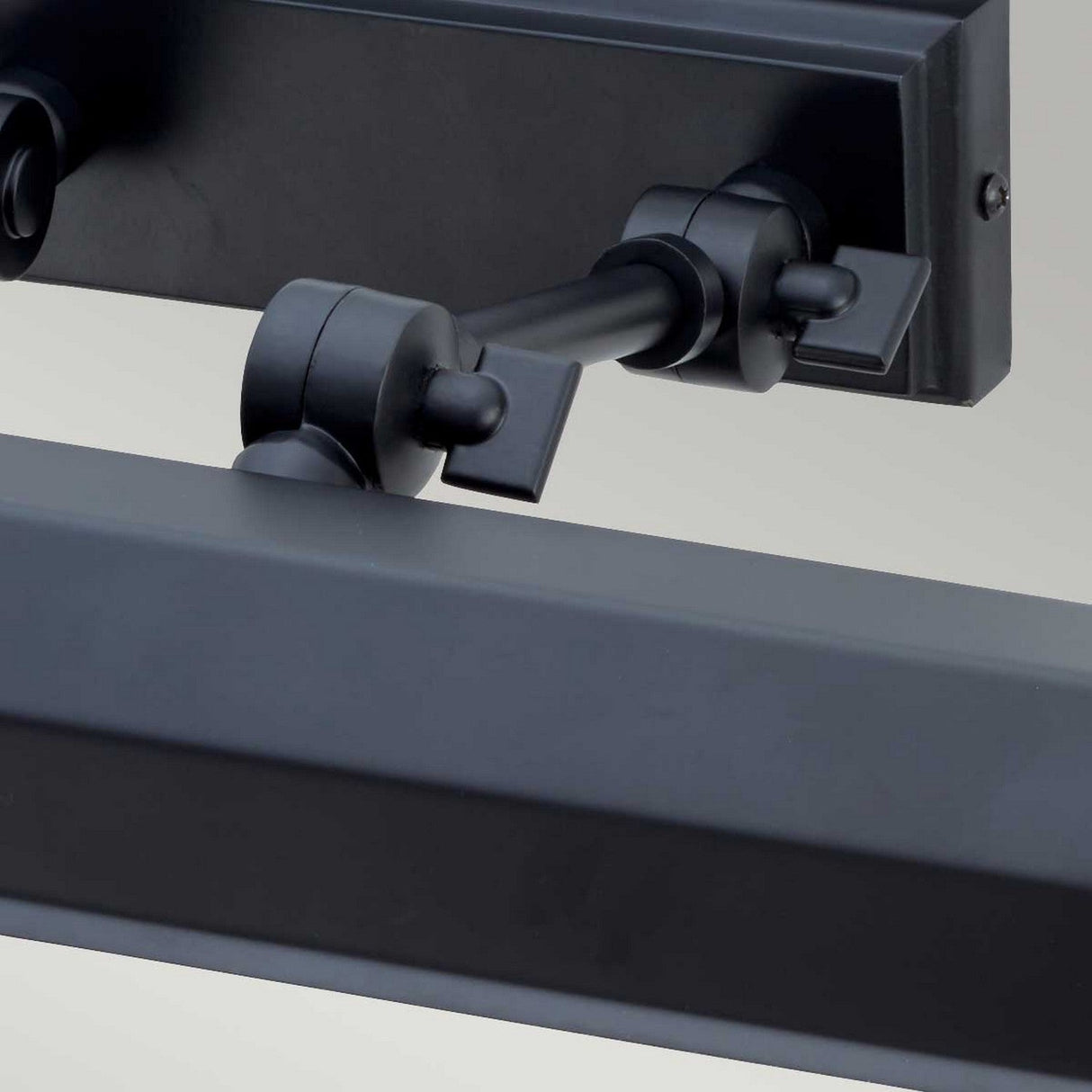 Close-up of a black hinge mechanism attached to a flat metal piece, showcasing adjustable knuckle joints and a cylindrical connector with a visible screw, set against a neutral backdrop. This modern design element is ideal for the Chawton Medium Picture Light - Black.