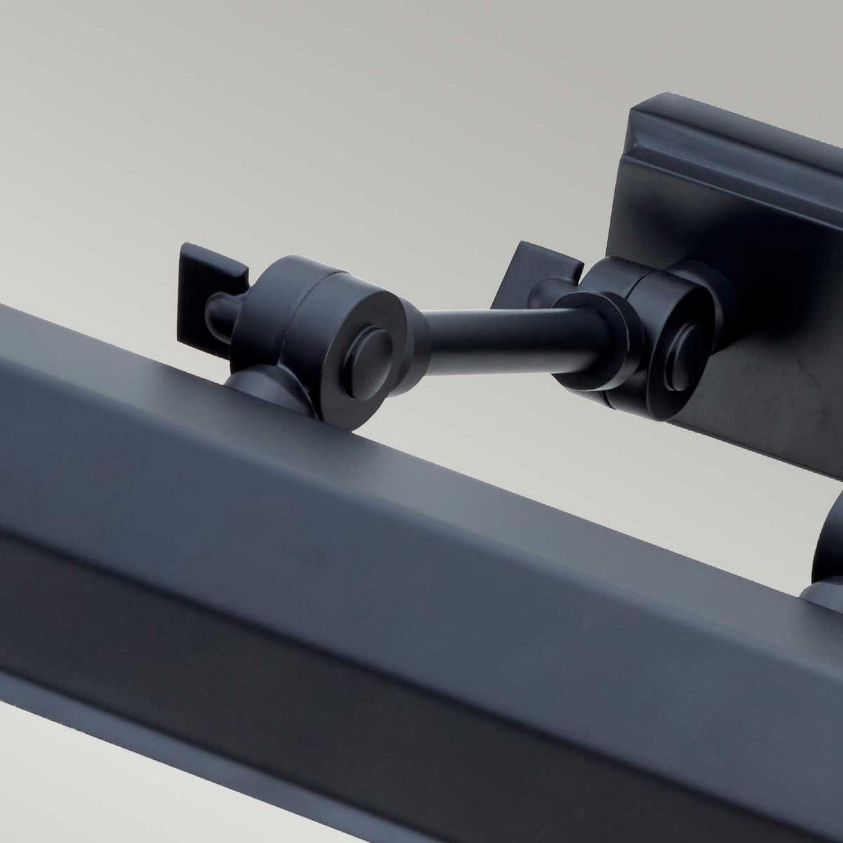 Close-up of a mechanical hinge with a sleek matte black finish, likely part of a sophisticated modern lighting design. The image features adjustable knuckle joints connecting to a pivoting component set against a neutral background, evoking the elegance of the Chawton Medium Picture Light - Black.