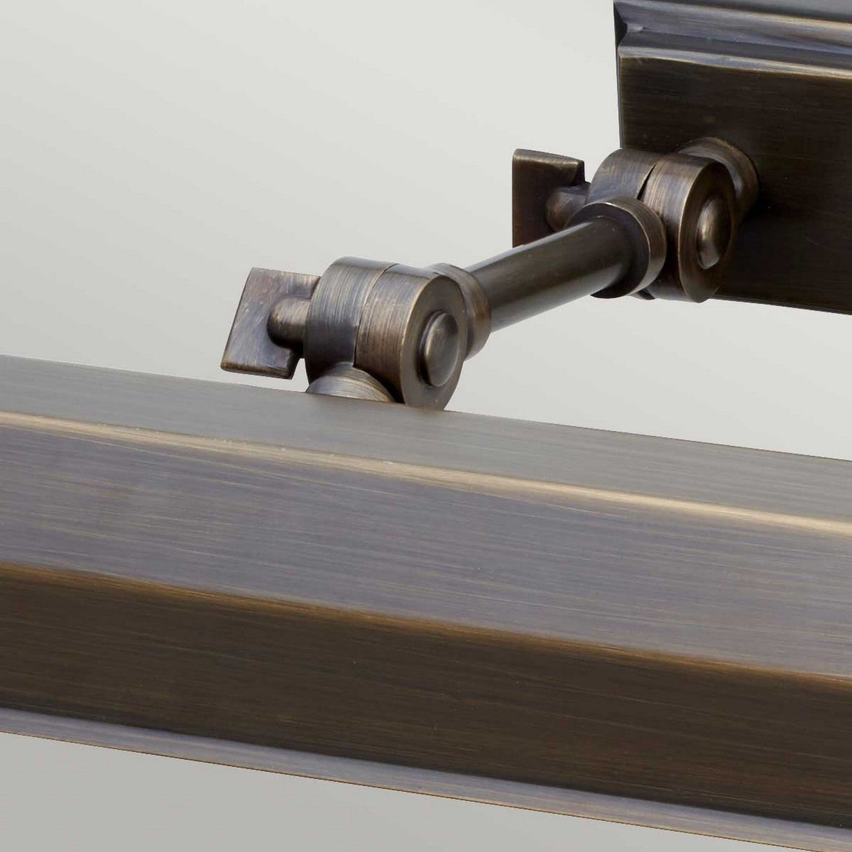 Close-up of a dark bronze-colored metal hinge with a rod connecting two segments, featuring a slightly textured surface. This hinge, reminiscent of the Chawton Medium Picture Light - Dark Bronze design, is part of a larger structure, set against a neutral background ideal for illuminating artwork.