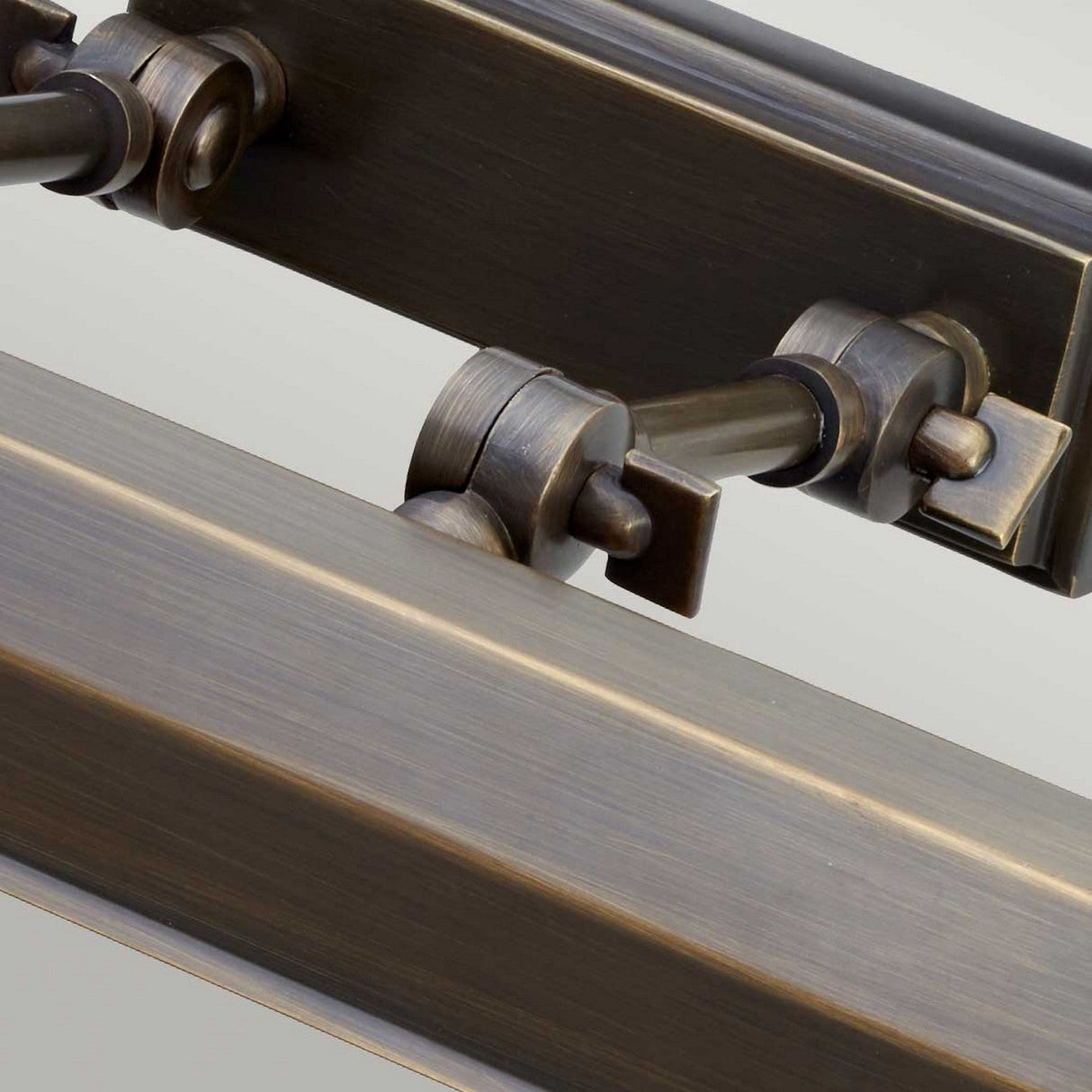 Close-up of the Chawton Medium Picture Light in dark bronze, featuring an industrial-style hinge mechanism. The image showcases two parallel cylindrical rods connected by joints, illuminated to highlight the intricate design and texture of the metal components.