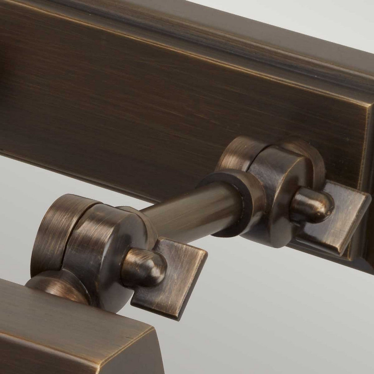 Close-up of a metal hinge featuring a dark bronze finish, connected by adjustable knuckle joints in a rustic, industrial design. The surface has a brushed texture that adds a vintage aesthetic similar to the Chawton Small Picture Light - Dark Bronze.