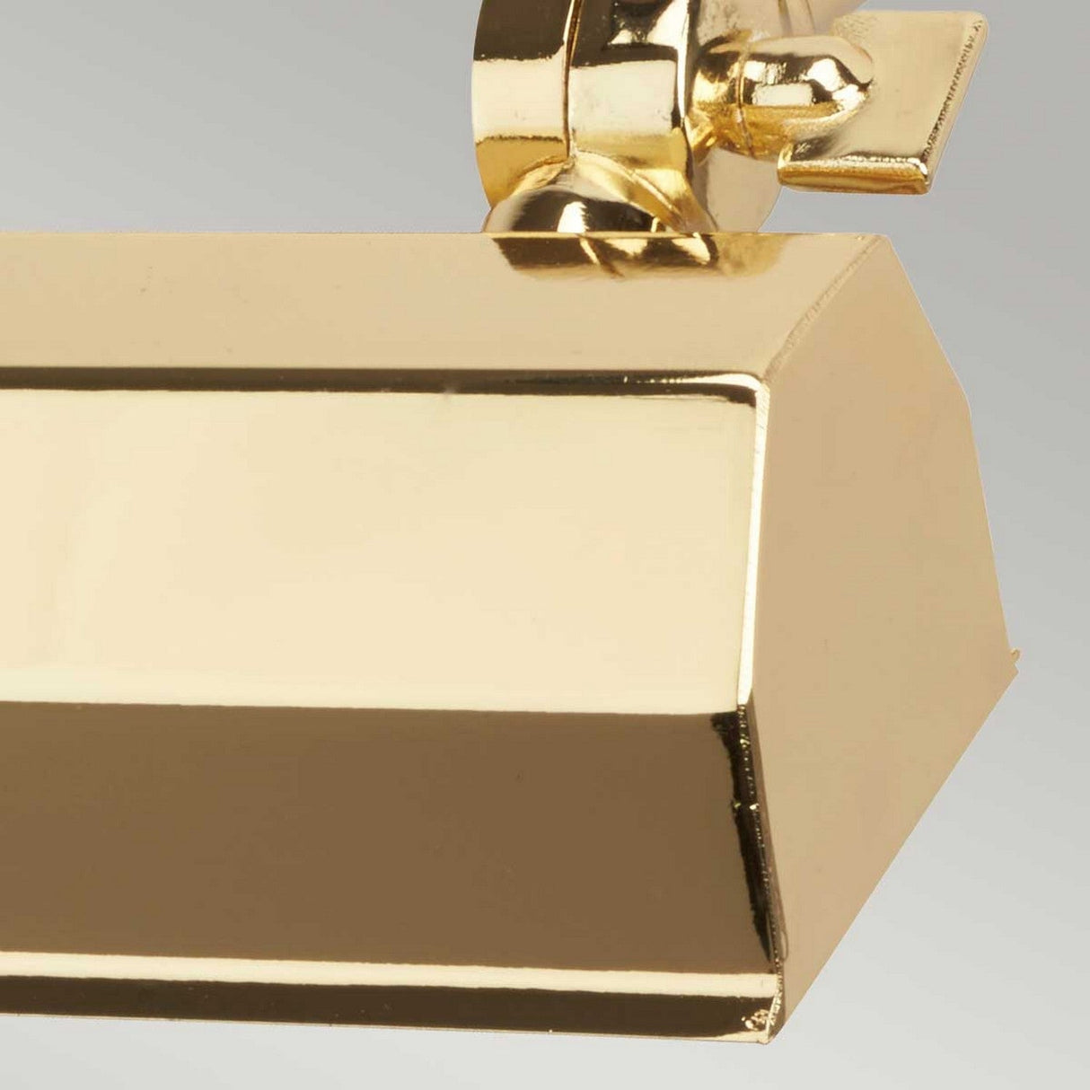 A close-up of the Chawton Small Picture Light - Polished Brass showcases its glossy finish and metal key-like adjuster at the top. It features adjustable knuckle joints and is set against a plain gray background.