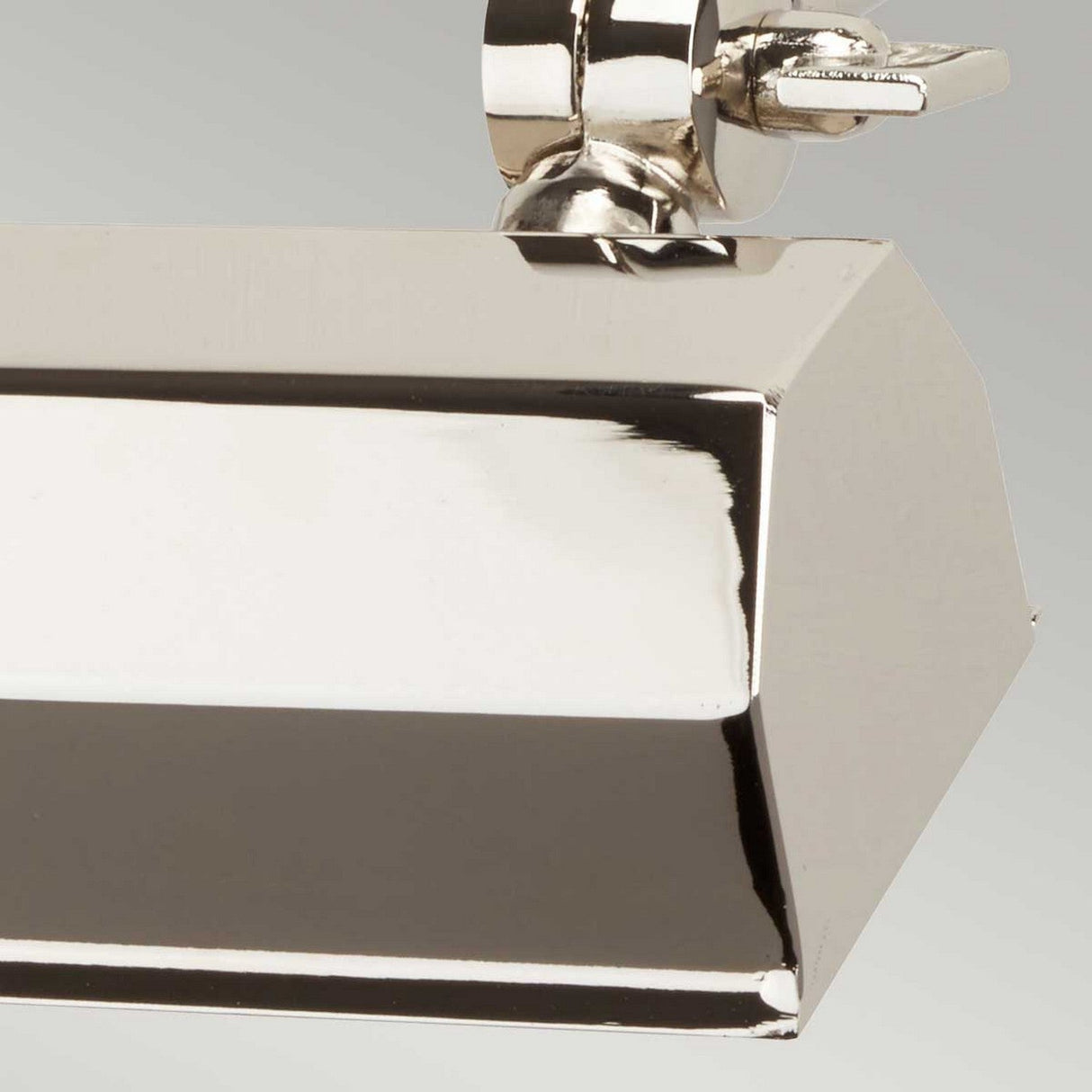 The close-up image showcases the Chawton Small Picture Light in a rectangular shape with an angular design, featuring a rounded fixture at the top and a small, round handle on the side. Its polished nickel finish presents a shiny metallic surface that reflects light effortlessly.