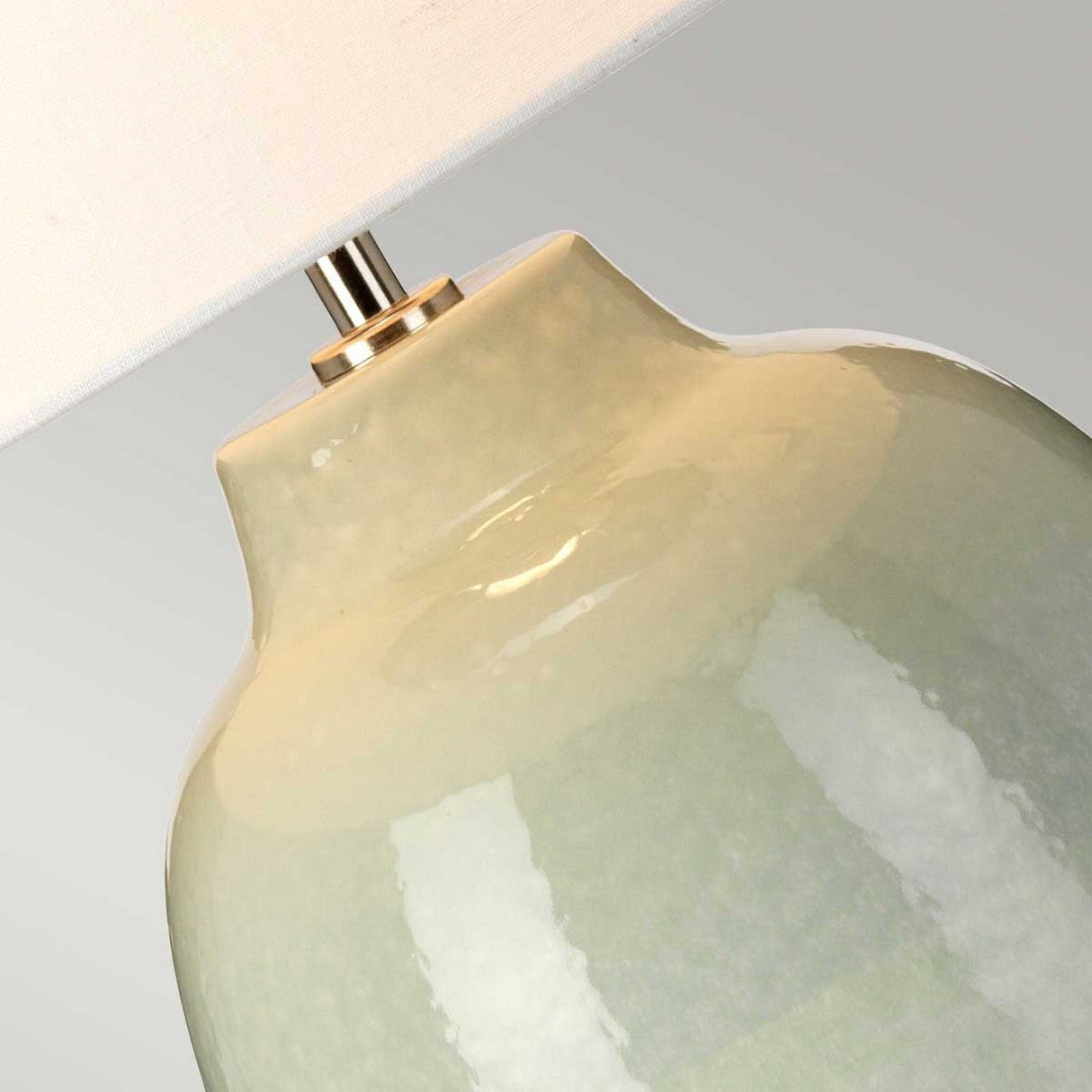 Close-up of the Chelsfield Table Lamp - Pale Green & White, showcasing a ceramic base with a glossy light green finish and a white lampshade. This lamp features a contemporary, sleek design with a minimalist appeal, complemented by a silver-toned neck that seamlessly connects the shade to the base.