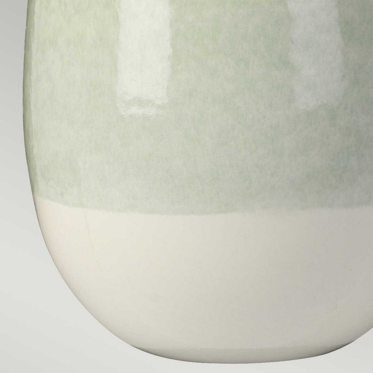 A close-up of a smooth, rounded ceramic vase featuring a soft gradient from light green to white beautifully captures the minimalist aesthetic. The vase has a glossy finish that subtly reflects light against a neutral grey backdrop, echoing the elegance of the Chelsfield Table Lamp's ceramic base in Pale Green & White.