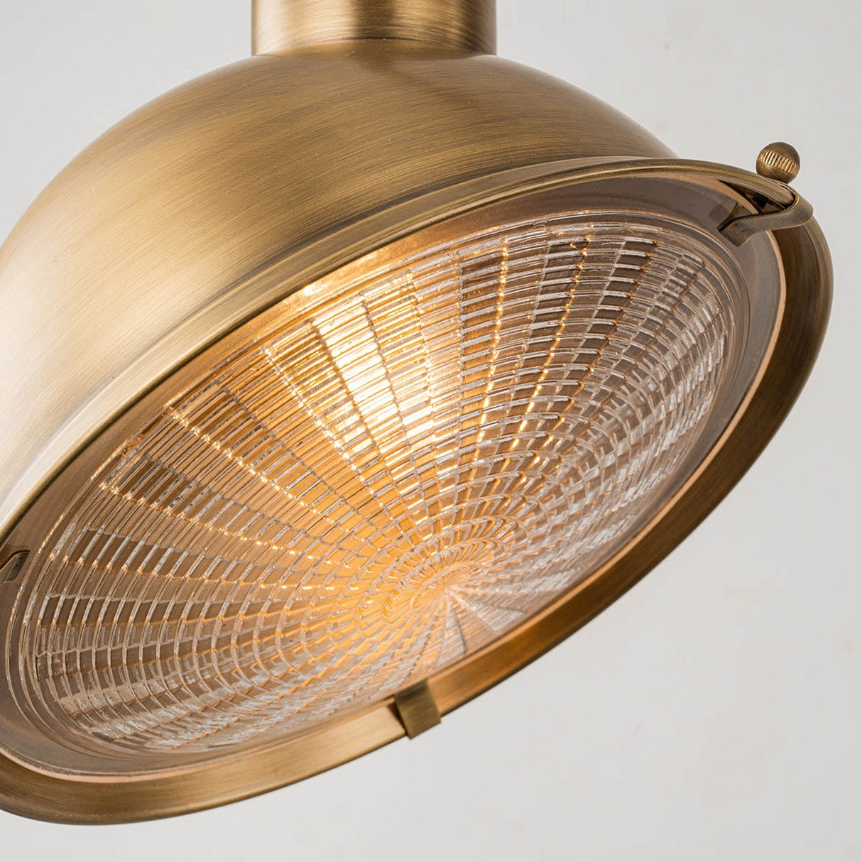 A close-up of the Chiswick Outdoor Brass Wall Light in an antique brass finish, featuring a ribbed glass shade that emits warm light. The fixture boasts a circular design with an elegant metallic finish, perfectly capturing a vintage industrial style against a neutral background.