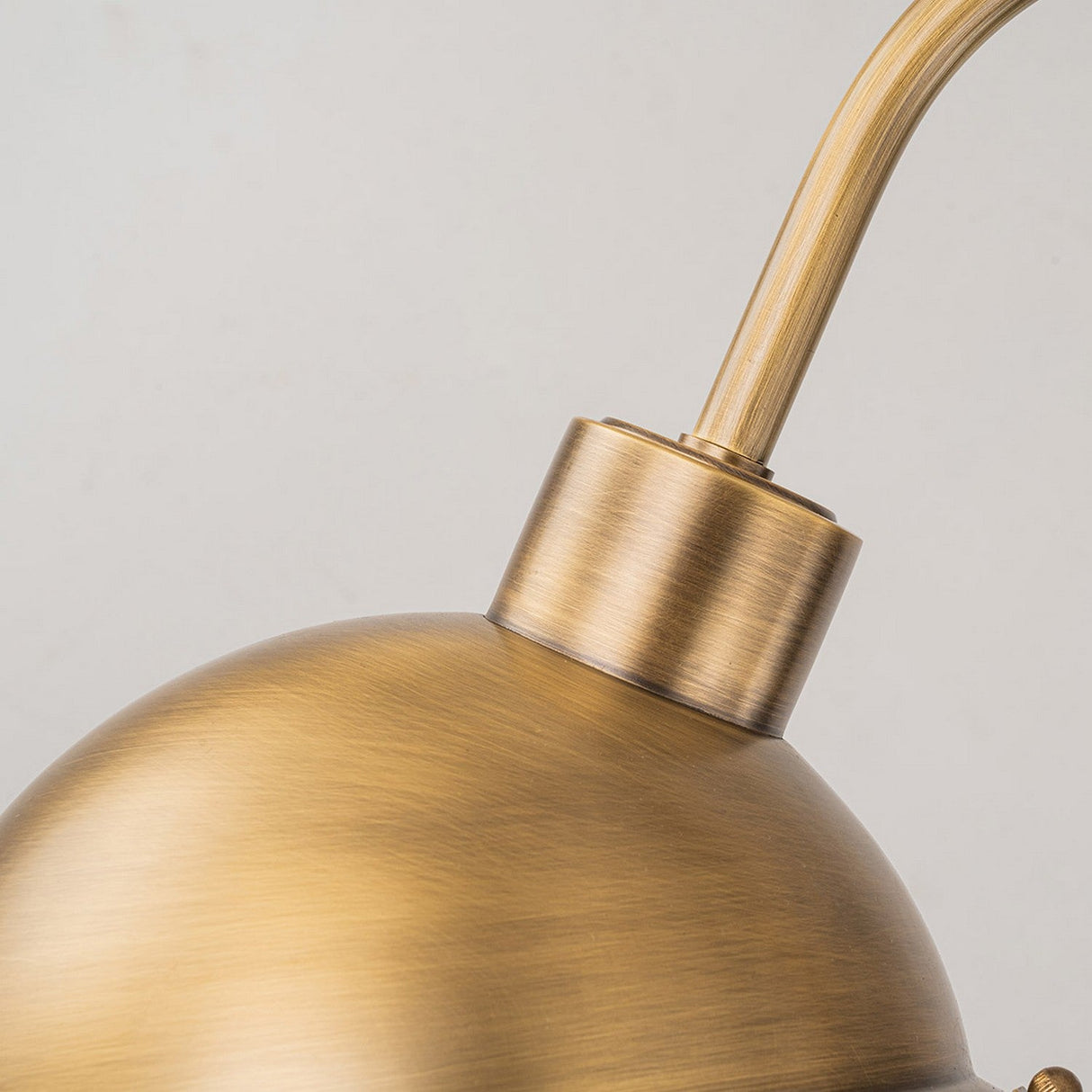 Close-up of the Chiswick Outdoor Brass Wall Light - Antique Brass showcasing a smooth, rounded shade and sleek, curved arm against a light gray background. Its antique brass brushed finish enhances the vintage-inspired elegance.