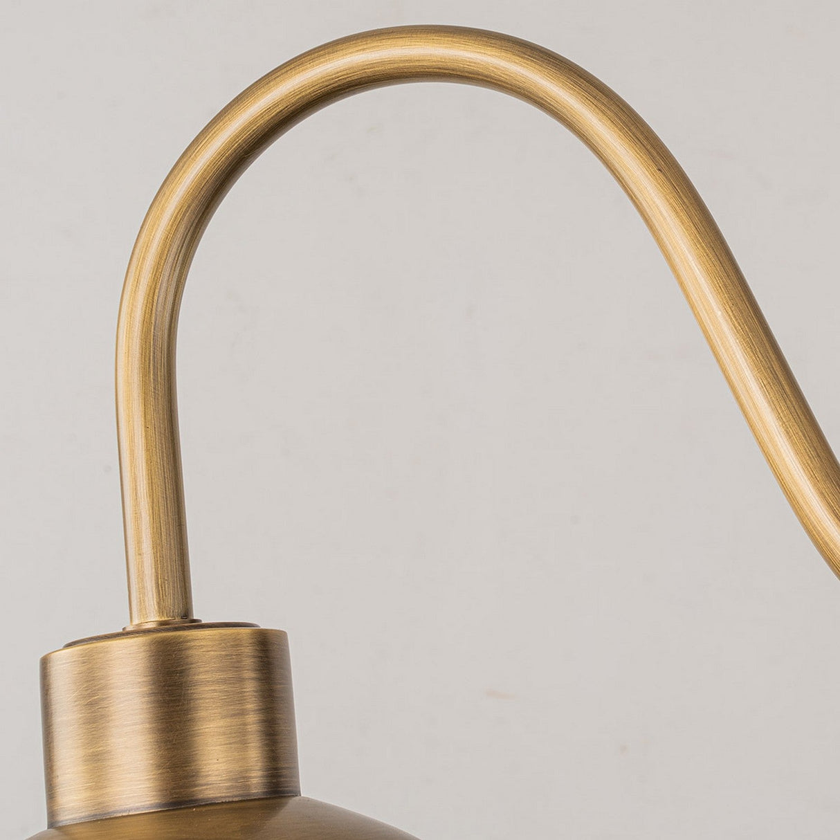 A close-up of the Chiswick Outdoor Brass Wall Light - Antique Brass highlights its curved arm and sleek, modern design against a plain gray background. This vintage-inspired fixture features a soft, brushed texture in antique brass.