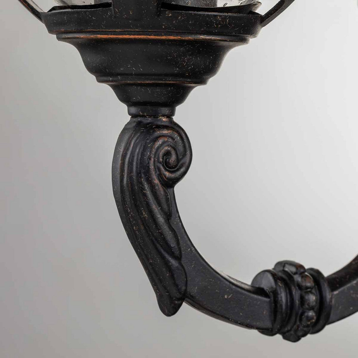 Close-up of the Cleveland-1 Outdoor Small Wall Lantern, showcasing its ornate dark metal scroll design with intricate detailing and a weathered bronze finish. The design includes curled elements and a textured surface, complemented by clear seeded glass to create a classic and elegant look suitable for an outdoor wall light.