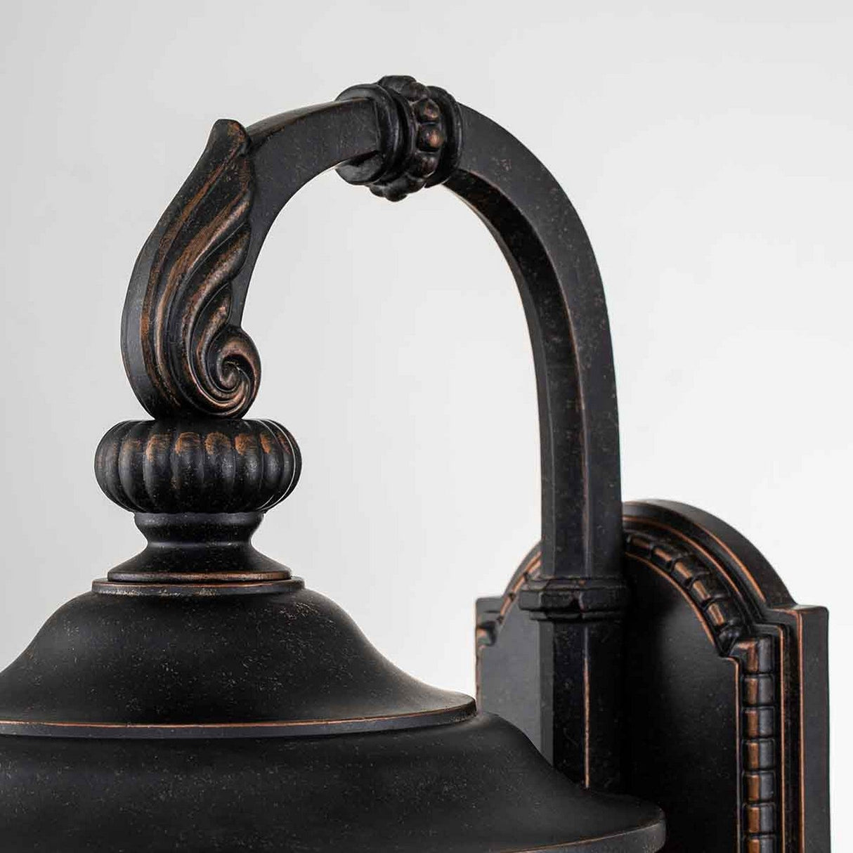A close-up view of the Cleveland-2 Outdoor Medium Wall Lantern reveals its vintage-style design, featuring intricate detailing and a gracefully curved arm. Its weathered bronze finish with subtle accents stands out against a white background, making it an ideal choice for enhancing outdoor spaces.