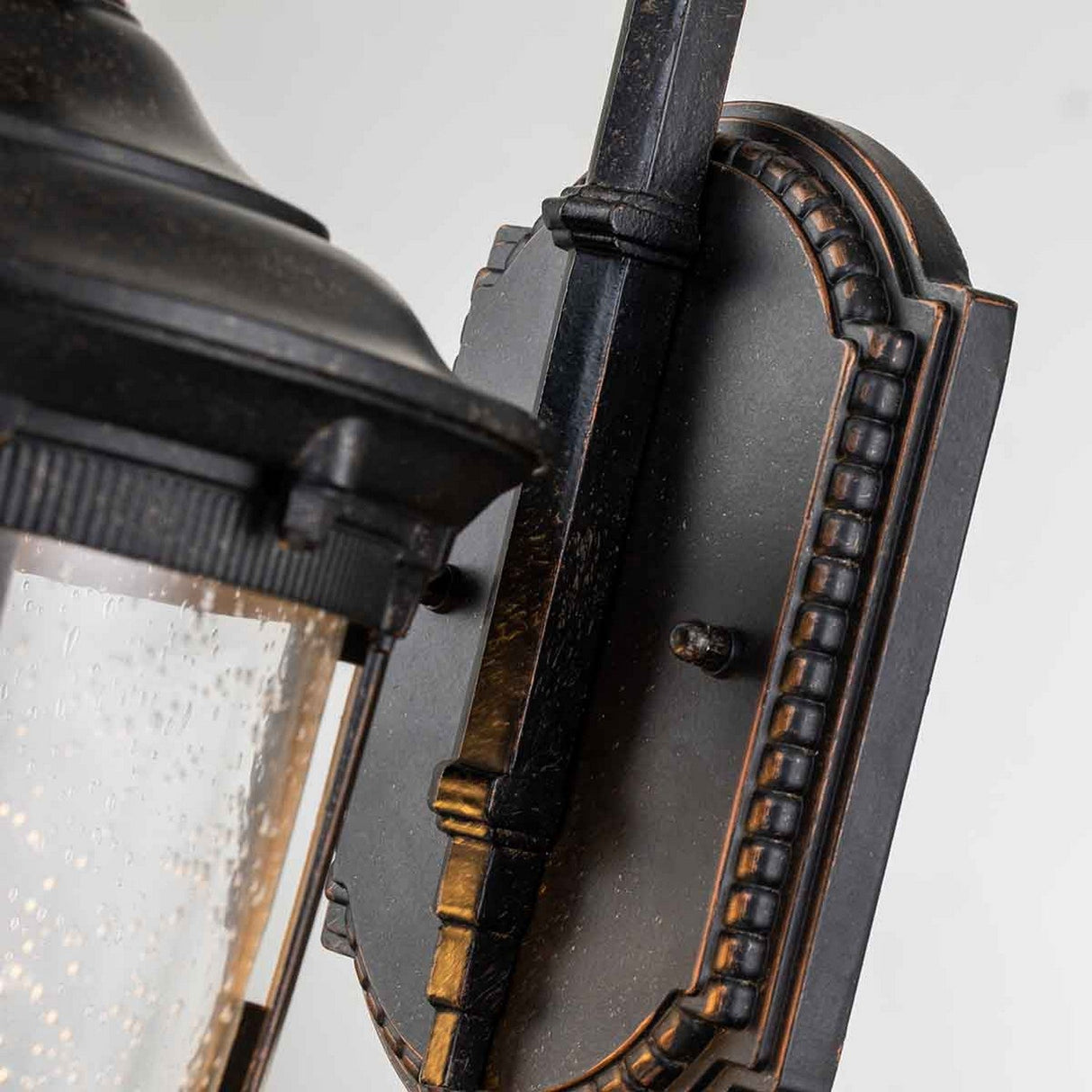 Here's a close-up of the Cleveland-2 Outdoor Small Wall Lantern in weathered bronze, showcasing its intricate detailing and textured glass cover. This wall-mounted lantern features ornate edging for a classic vintage style and is designed with an IP44 rating to withstand the elements.
