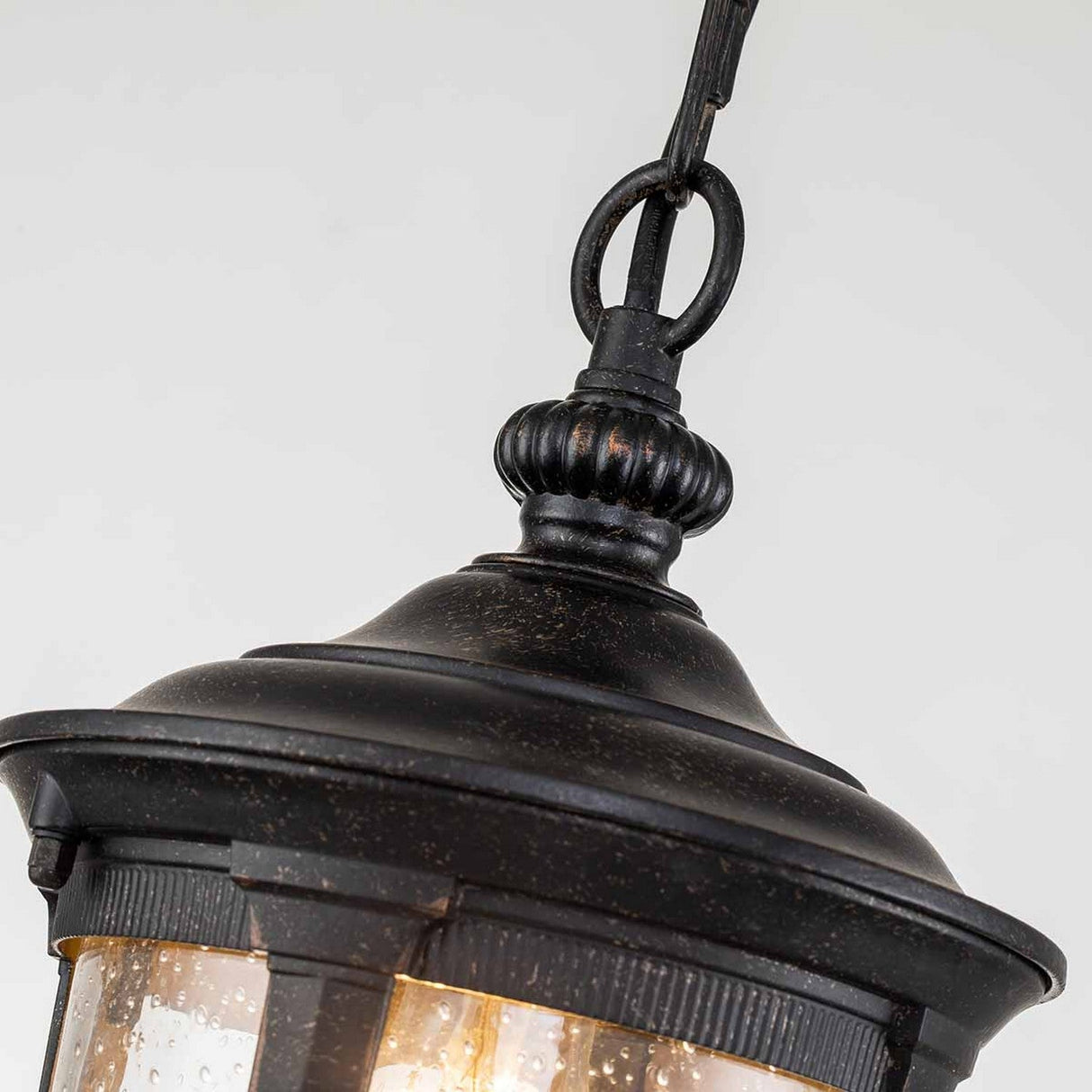 Close-up of the Cleveland Outdoor 1 Light Small Chain Pendant in weathered bronze, showcasing its decorative metal top and hanging loop. The pendant features a glass enclosure with a visible bulb inside, all enveloped by a textured surface. Set against a plain light gray background, the design's elegance is highlighted beautifully.