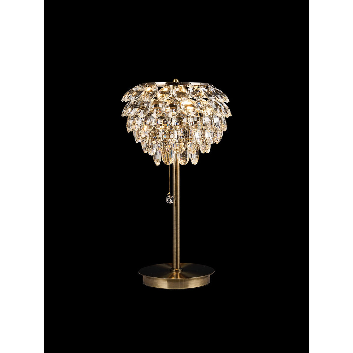 The Coniston 2 Light Crystal Table Lamp in antique brass features a round base and a layered crystal-effect shade for a shimmering, elegant look that stands out boldly against a black background.