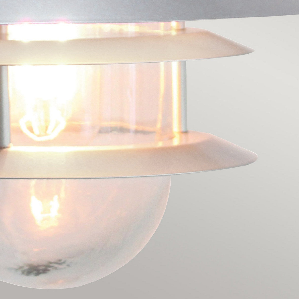 Here's a rewritten version of the sentence based on the given product data:
"Close-up of the Copenhagen Outdoor Wall Lantern - Silver, featuring a glowing bulb within a cylindrical glass shade accented by stainless steel rings. The Scandinavian design highlights a sleek, minimalist aesthetic with soft illumination.