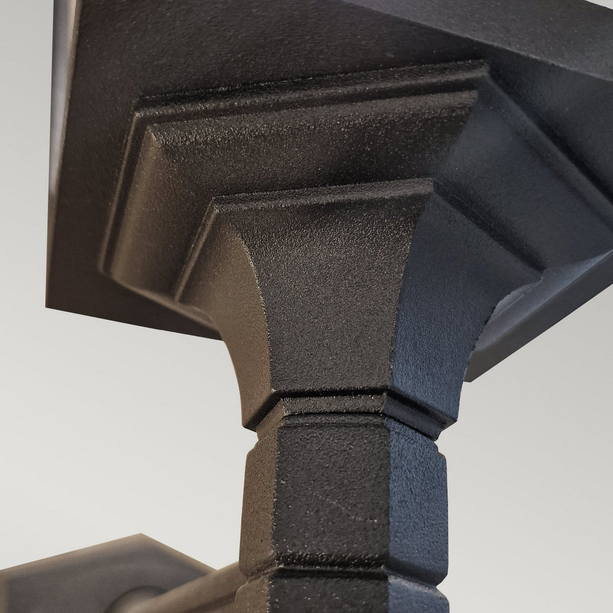 Close-up of a Chapel 1 Light Outdoor Up Wall Lantern in black, showcasing its textured design crafted from die-cast aluminum with square and angular features. This modern, robust lantern emphasizes its ridged patterns and symmetrical shapes, making it ideal for outdoor lighting with an IP44 rating. The background is a soft, neutral tone.