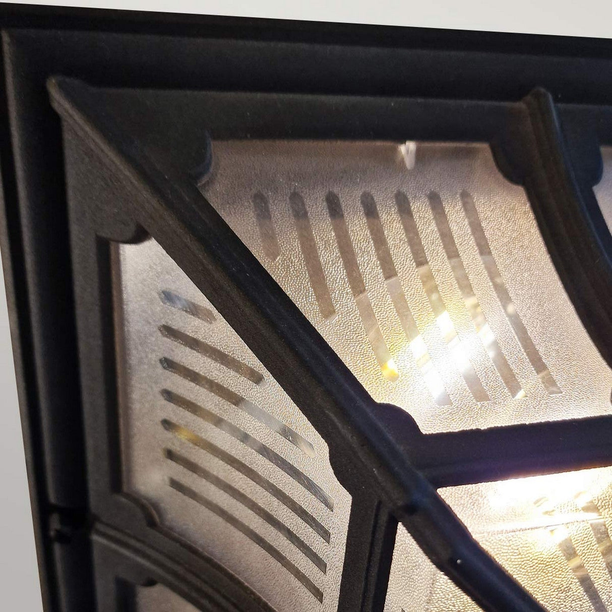Close-up of the Chapel 1 Light Outdoor Flush Light in black, featuring a frosted glass cover illuminated from within. Made from die-cast aluminum, the geometric pattern on the glass diffuses the light beautifully, casting warm glows and shadow effects. Its IP44 rating ensures it is ideal for weather-resistant outdoor use.