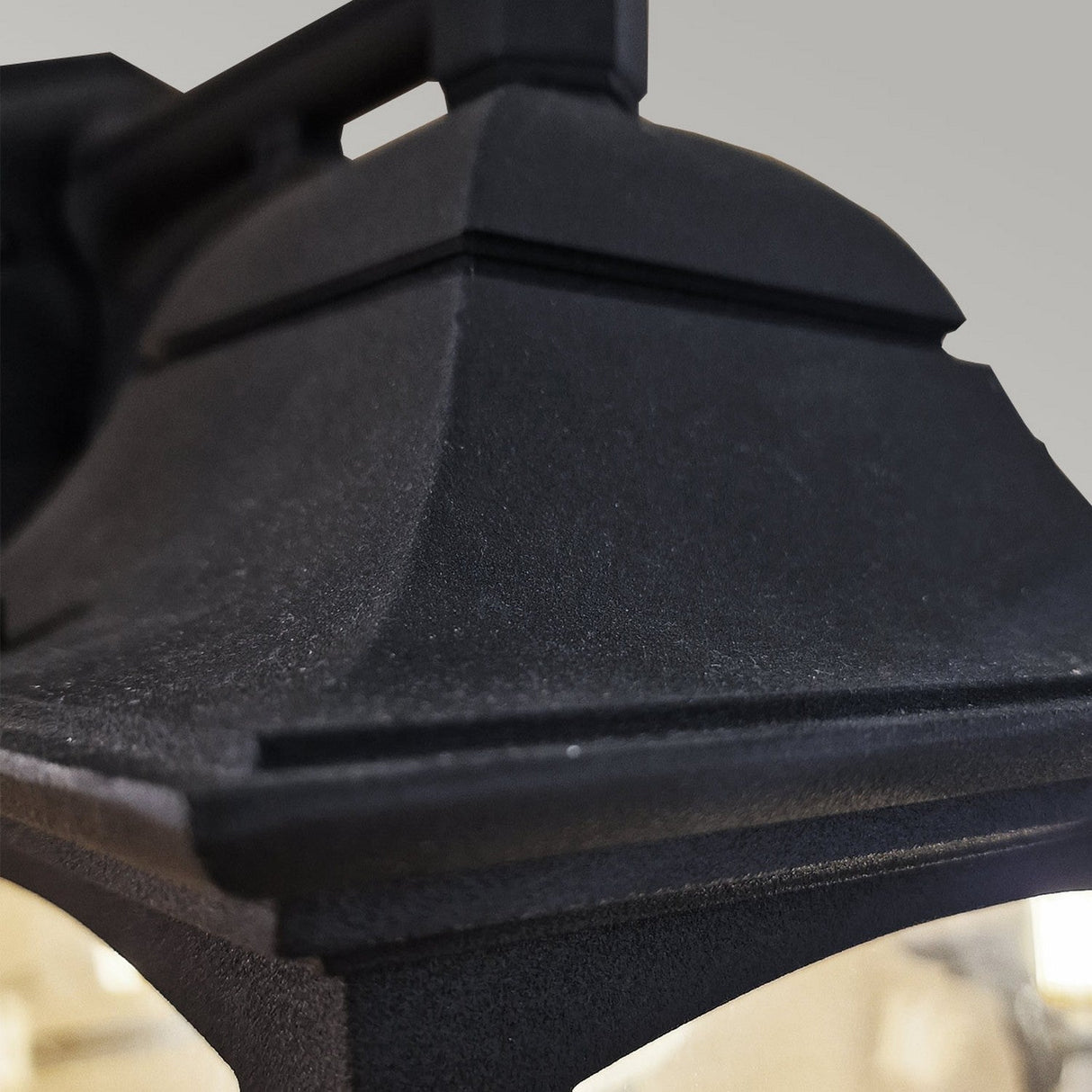 Close-up of the top corner of the Chapel 1 Light Outdoor Down Wall Lantern in a black finish, featuring a peaked design and clear glass panes. The focus is on the textured black metal surface, highlighting its IP44 rating against a neutral background.