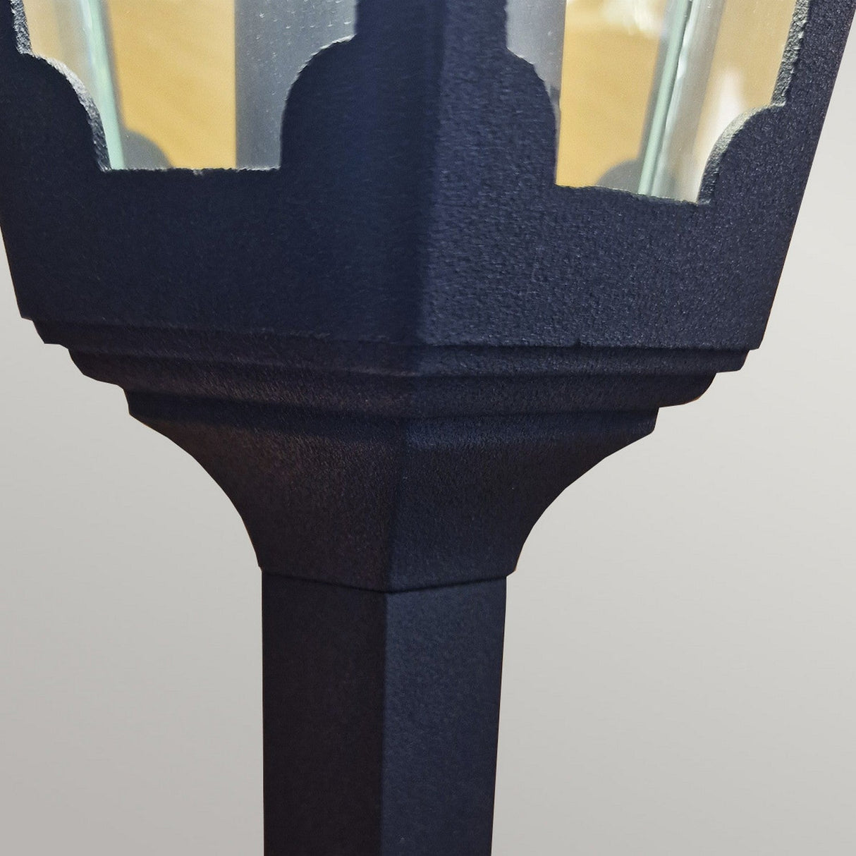 Close-up of the Chapel 1 Light Pillar Lantern in black, featuring a textured surface and a classic design made from durable die-cast aluminum. The metal frame encases clear glass panels, making it perfect for outdoor lighting. It has an IP44 rating, which ensures enhanced protection against the elements.