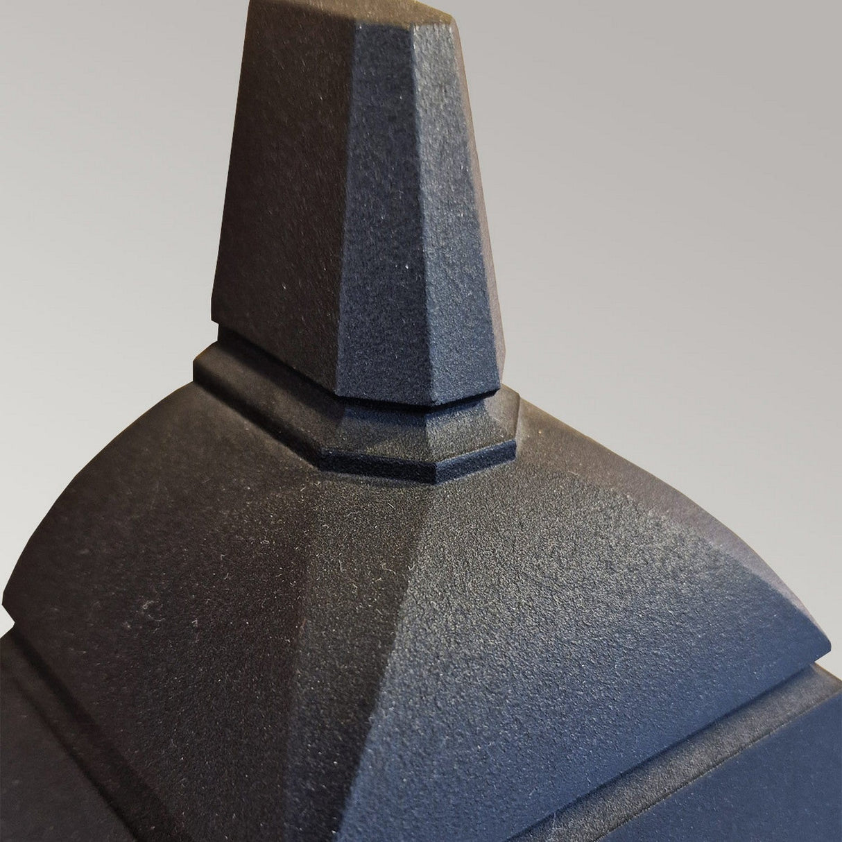 Close-up of the Chapel-1 1 Light Outdoor Wall Lantern in black, showcasing its dark, angular structure crafted from sleek die-cast aluminum. The design features geometric, stepped shapes reminiscent of a modern half-lantern sculpture set against a neutral background, highlighting the elegance of this outdoor wall light.