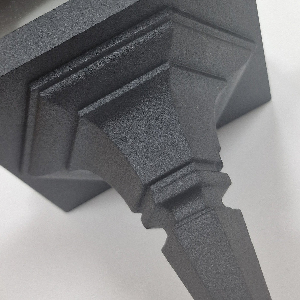 Close-up of a textured, dark metallic Chapel 1 Light Outdoor Chain Pendant in black, crafted from die-cast aluminium. The pendant's design features geometric shapes and angular lines tapering to a point, embodying a sharp and modern style, set against a plain, light background.