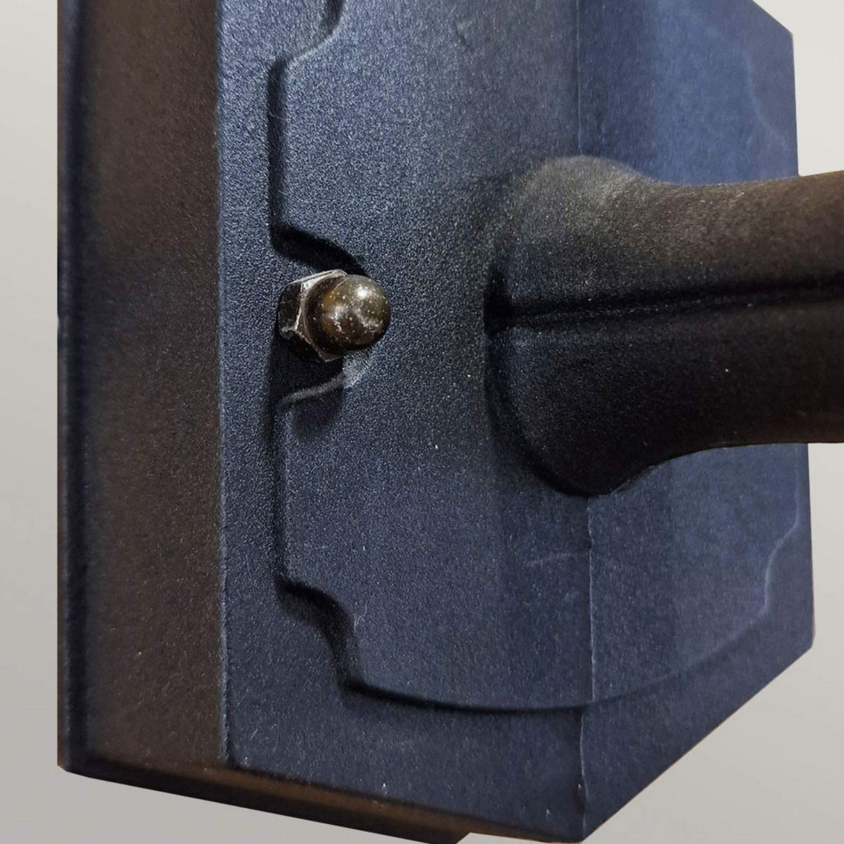 Close-up of a sleek, black wall-mounted bracket from the Chapel 1 Light Outdoor Mini Up Wall Lantern, meticulously crafted from durable die-cast aluminium featuring a visible bolt on the side. This image emphasizes the texture and design against a minimalist background.