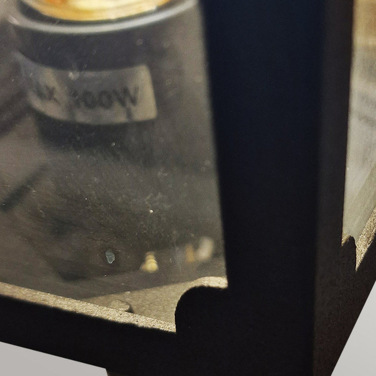 Close-up of the Chapel 1 Light Outdoor Mini Up Wall Lantern, showcasing the corner of its glass housing with a visible bulb labeled Max 100W. This black wall light features a dark, textured finish and is crafted from die-cast aluminum.