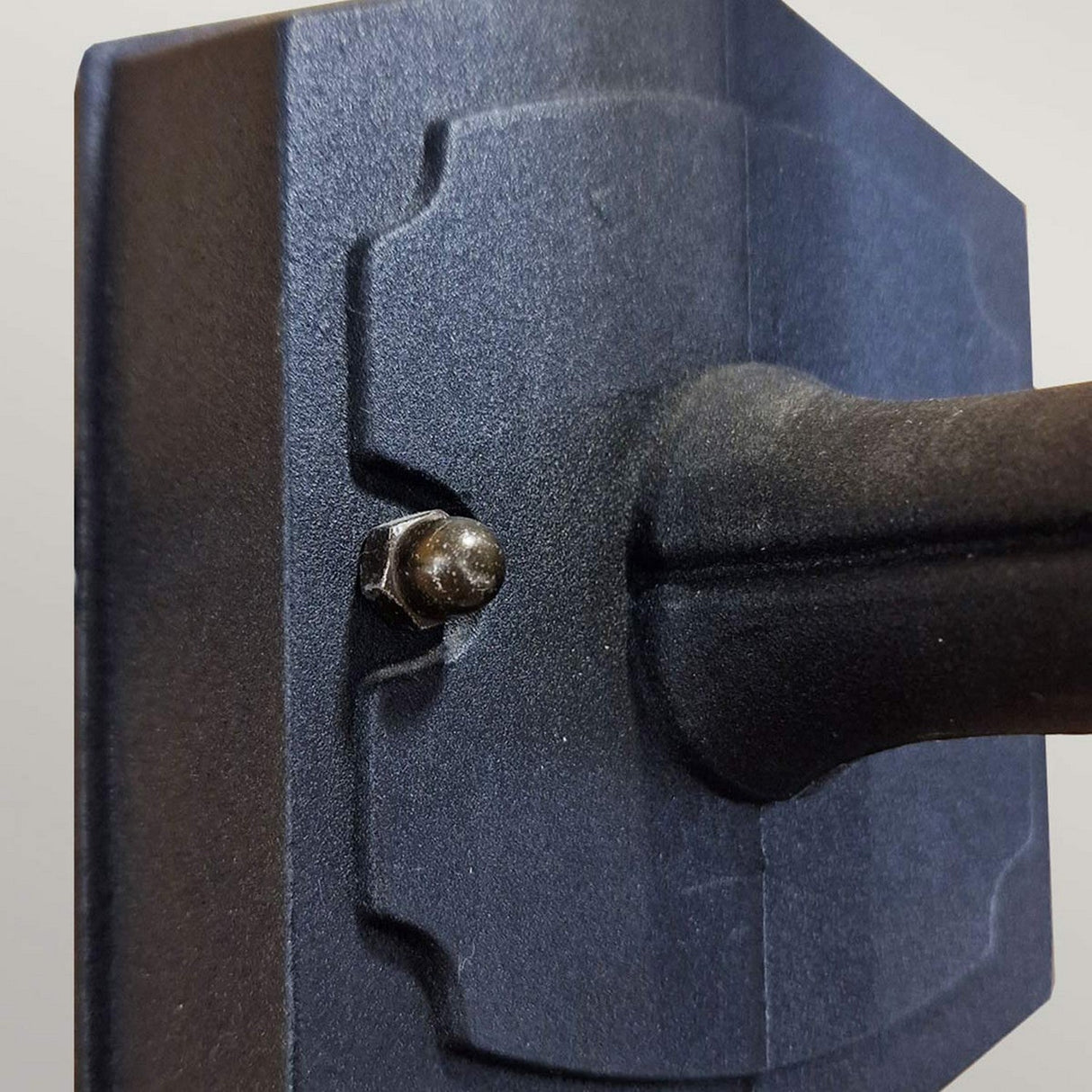 Close-up image of the Chapel 1 Light Outdoor Mini Down Wall Lantern in black, showcasing its sleek design similar to die-cast aluminum. A bolt secures the fixture to its mounting point, with a blurred background highlighting this connection.