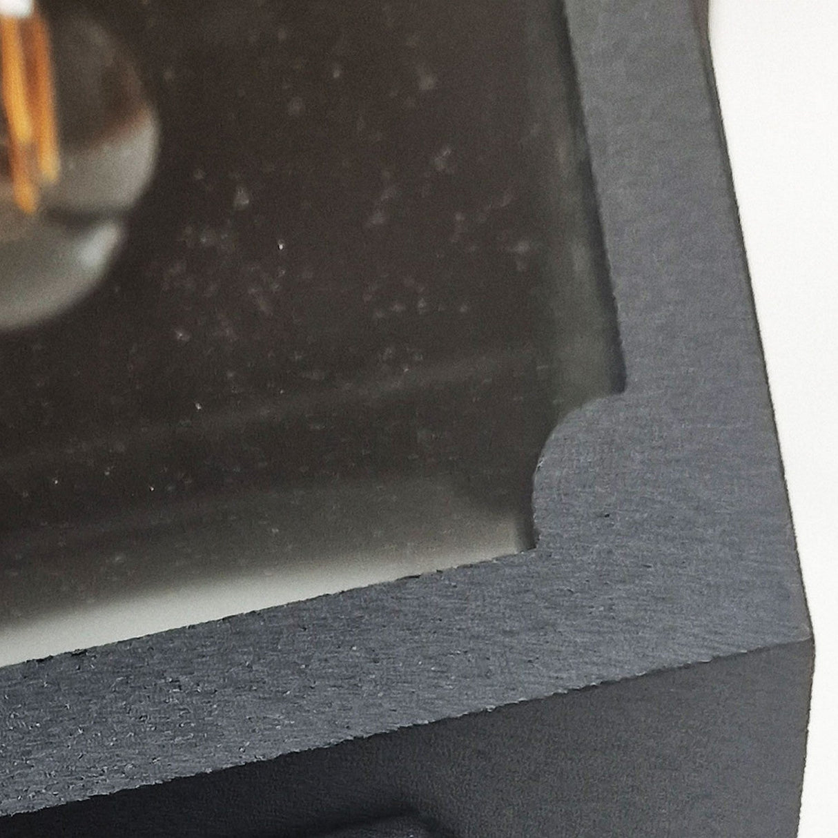 Close-up of the Chapel 1 Light Outdoor Mini Down Wall Lantern in black, featuring a transparent cutout that partially reveals reflective outdoor lighting within. The edge of the lantern’s black frame, which boasts an IP44 weather resistance rating, is highlighted with its textured finish. Most of the contents inside remain obscured from view.