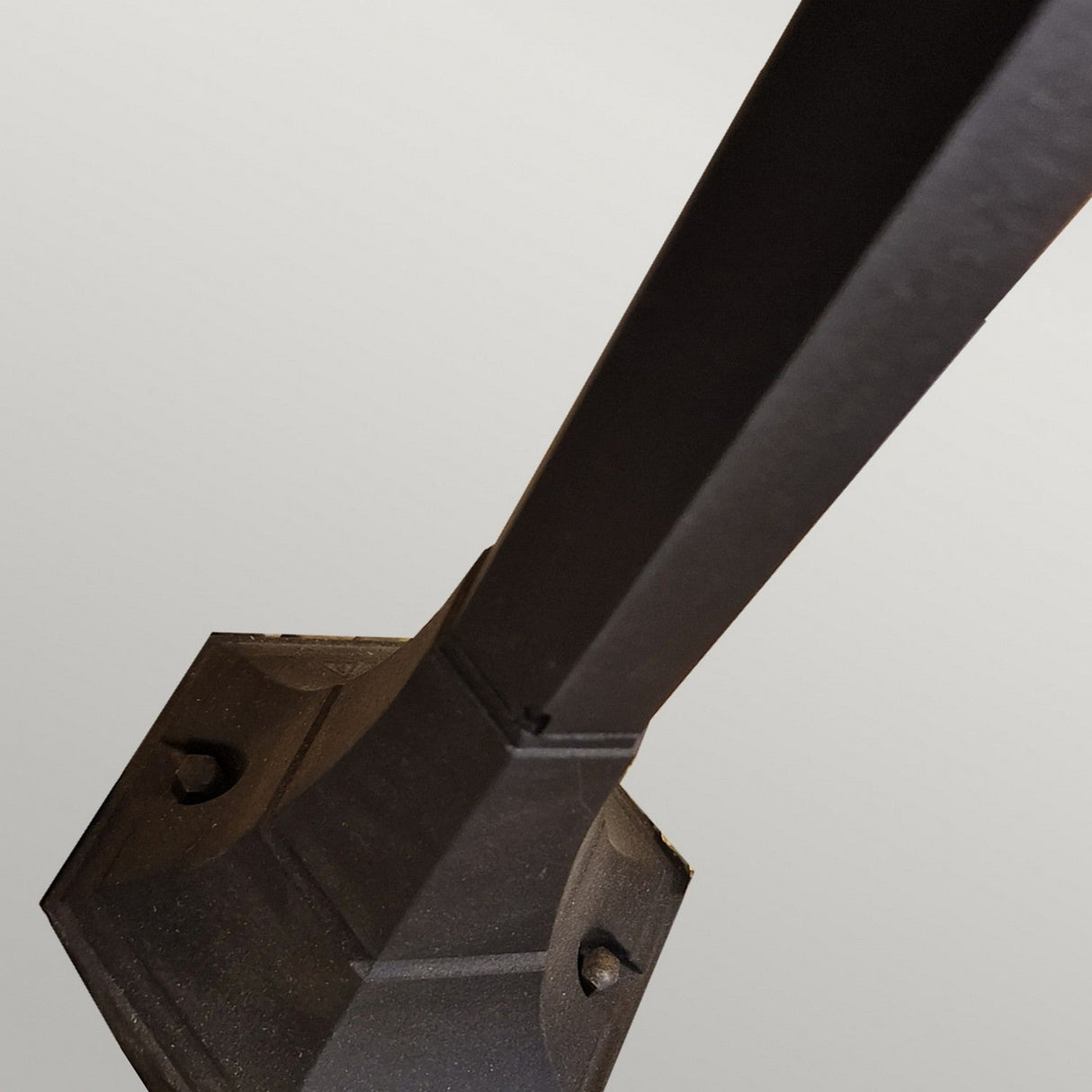 Close-up view of the Chapel 1 Light Mini Pillar Lantern in black, crafted from die-cast aluminum with a square base, shown against a simple gray background. The angle of the image highlights the lantern's height and shadowed contours, evocative of an elegant mini pillar.