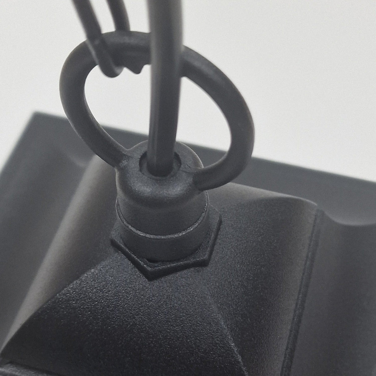 Close-up of a black metal hook, likely from the Chapel 1 Light Outdoor Mini Chain Pendant, made of die-cast aluminum, attached to a textured, angular surface, with two wires looped through the ring.