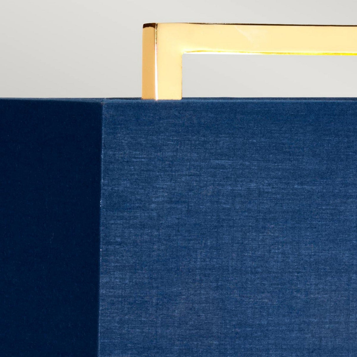 Close-up of a textured dark blue surface with a sleek, polished gold base extending from the top. The gold bar contrasts with the fabric-like material, creating a modern and stylish appearance reminiscent of the Cross Table Lamp With Blue Shade - Polished Gold.