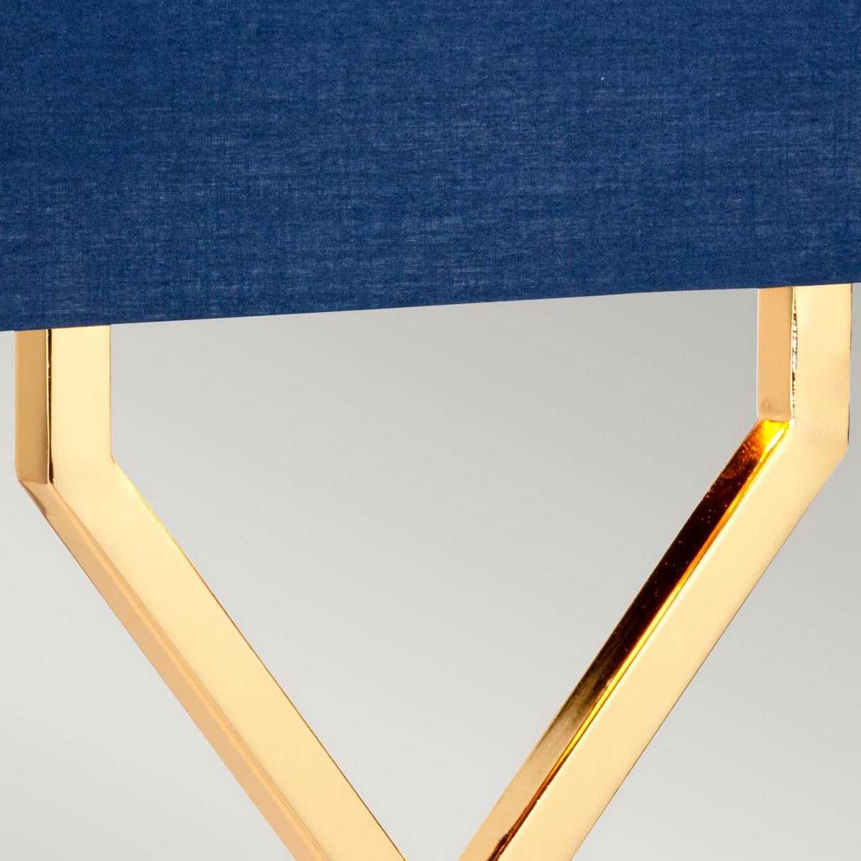 Close-up of a modern polished gold base with a geometric design supporting a navy blue tabletop. The neutral gray background highlights the sleek contrast between the glossy gold finish and matte blue surface, perfectly complementing the Cross Table Lamp With Blue Shade - Polished Gold.