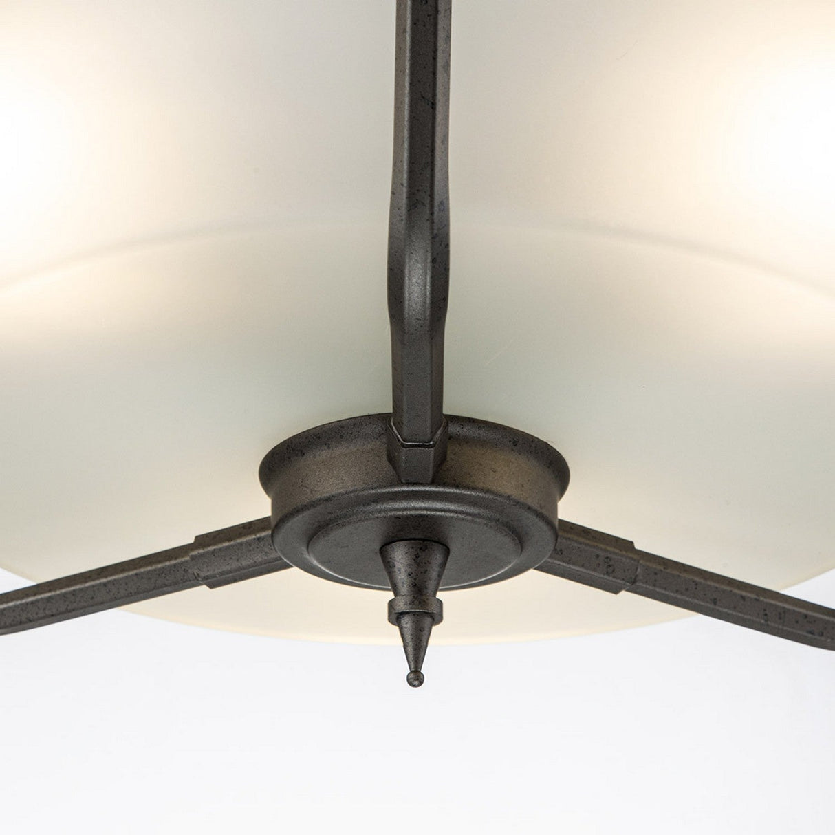 Detailed view of the Crown 3 Light Semi Flush - Graphite, designed with a brushed metal finish. This lighting fixture boasts a central round base and three supporting arms, enhanced by frosted glass shades that gently diffuse the light, highlighting its modern and minimalist architectural style.