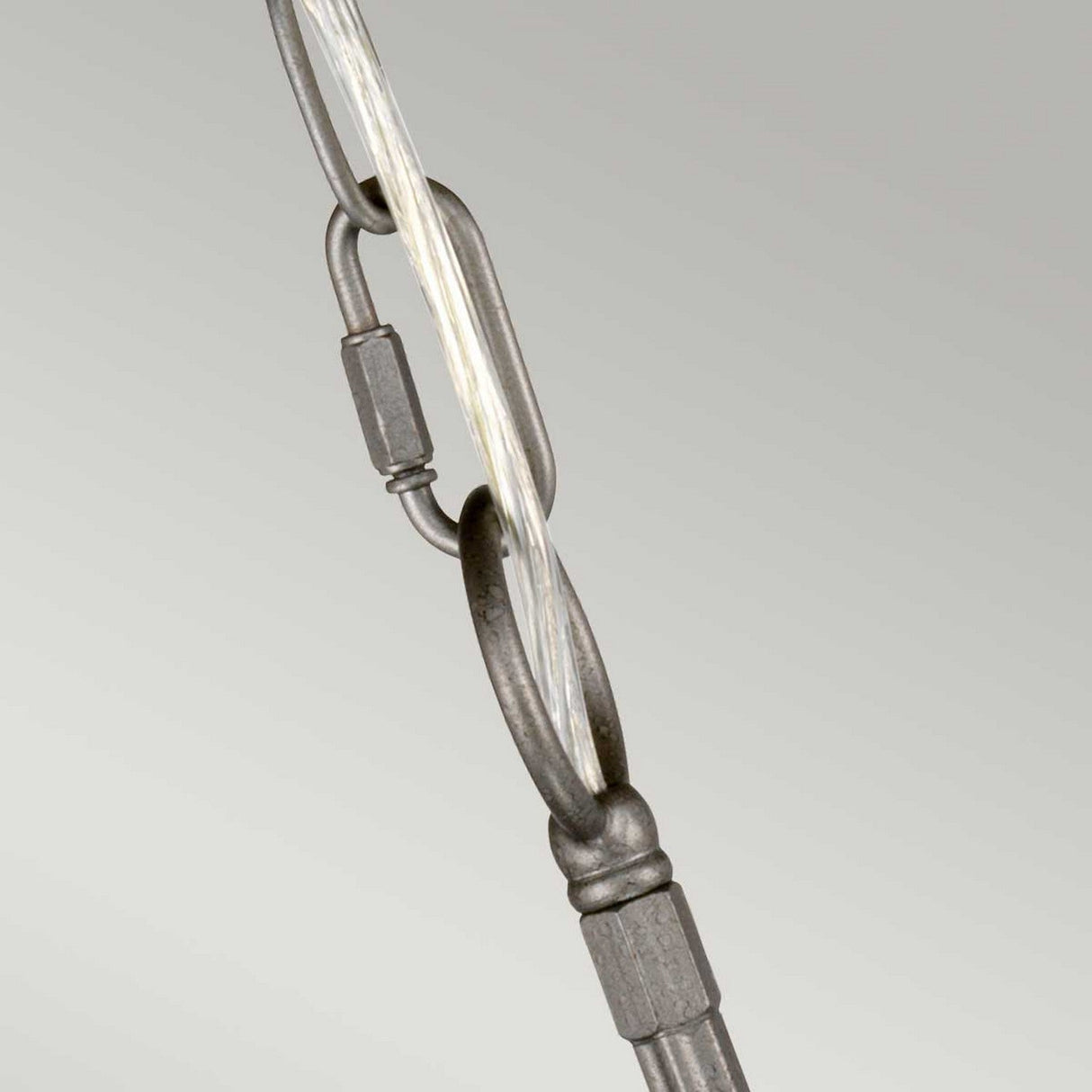 A close-up of a metal chain link connected to a twisted cable evokes regal elegance, much like the Crown 6 Light Chandelier in Graphite. The industrial design is gracefully set against a neutral, light gray background, resembling understated sophistication.