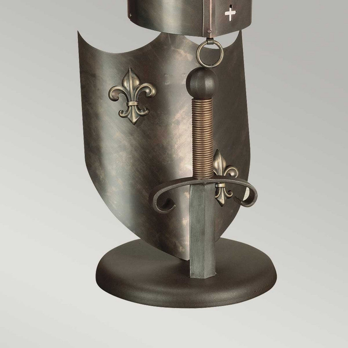 The Crusader Table Lamp - Burnished Bronze is a medieval-themed metal sculpture that includes a shield adorned with fleur-de-lis symbols and an upright sword on a round base. The sword's hilt features a coiled grip with curved quillons, and the shield showcases exquisite burnished bronze craftsmanship.