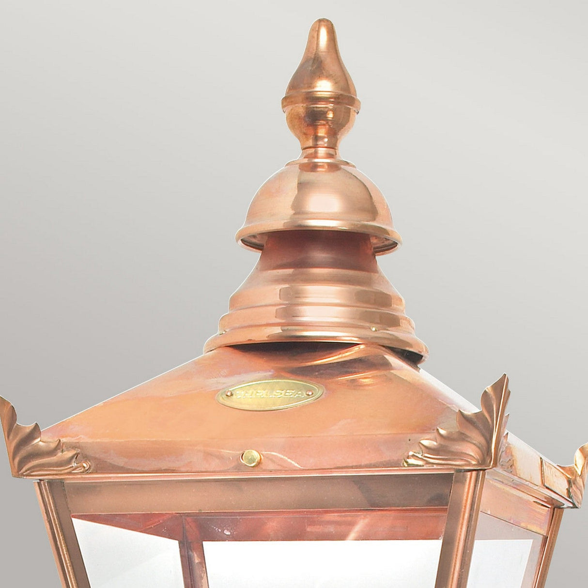Close-up of the Chelsea Outdoor 1 Light Wall Lantern in copper, showcasing its classic design elements with a decorative top and clear glass panels, set against a light gray background.