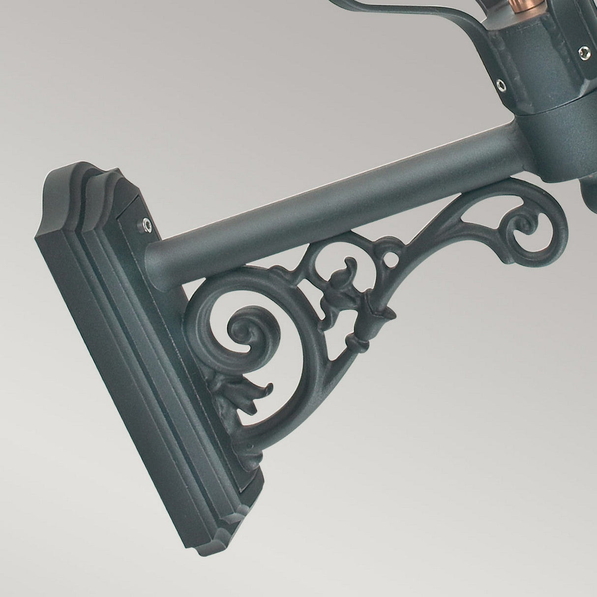 This exquisite black metal bracket features an intricate scrollwork design and a mounting plate, serving as the perfect support for the Chelsea Outdoor 1 Light Wall Lantern in Copper. The subtle gradient background accentuates the bracket's decorative elements, making it a superb choice for outdoor lighting with a classic aesthetic.