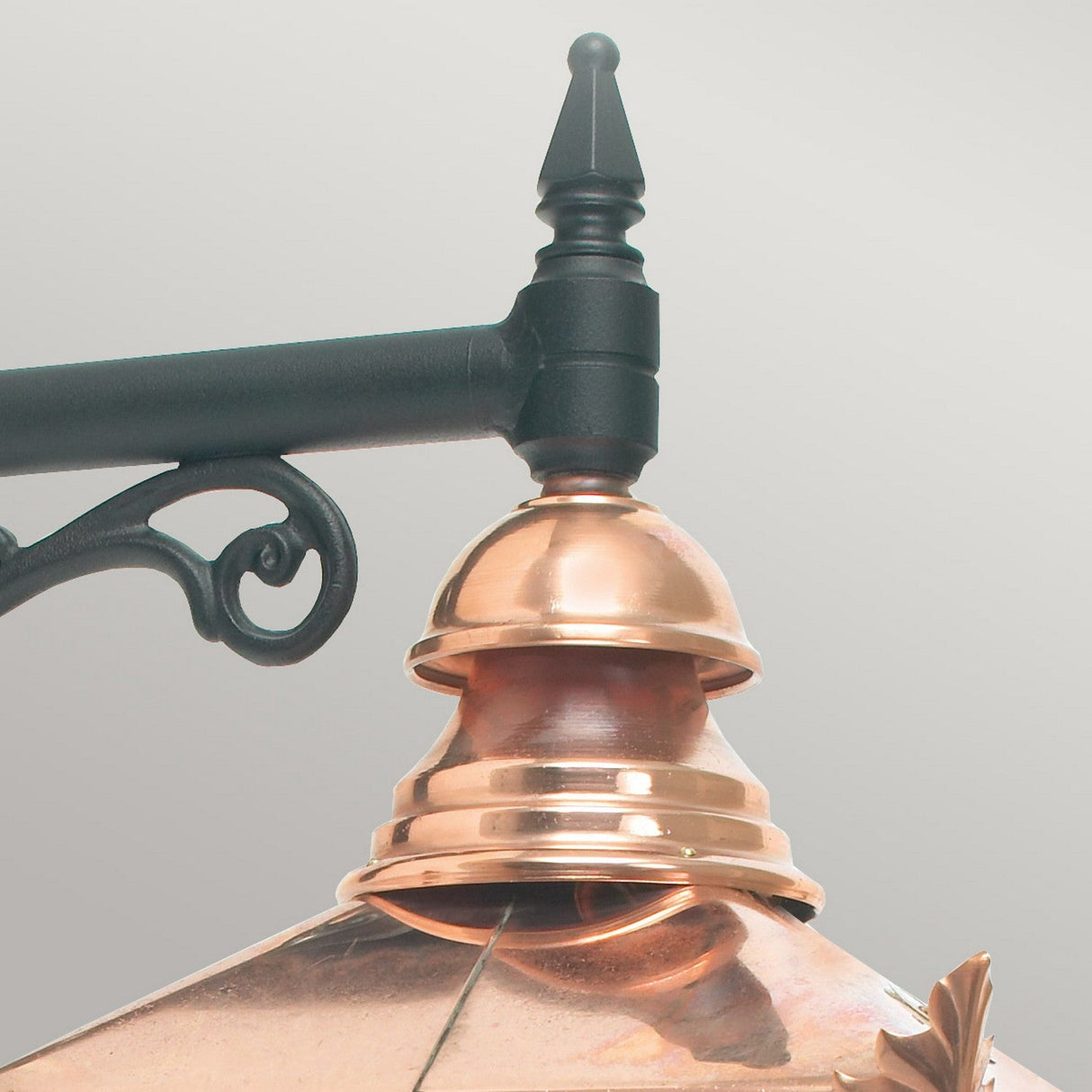 Close-up of the Chelsea Outdoor 1 Light Down Wall Lantern in copper, showcasing its decorative top finial and ornate black metal bracket. This elegant exterior decor lighting piece features intricate detailing and a polished finish against a neutral background.